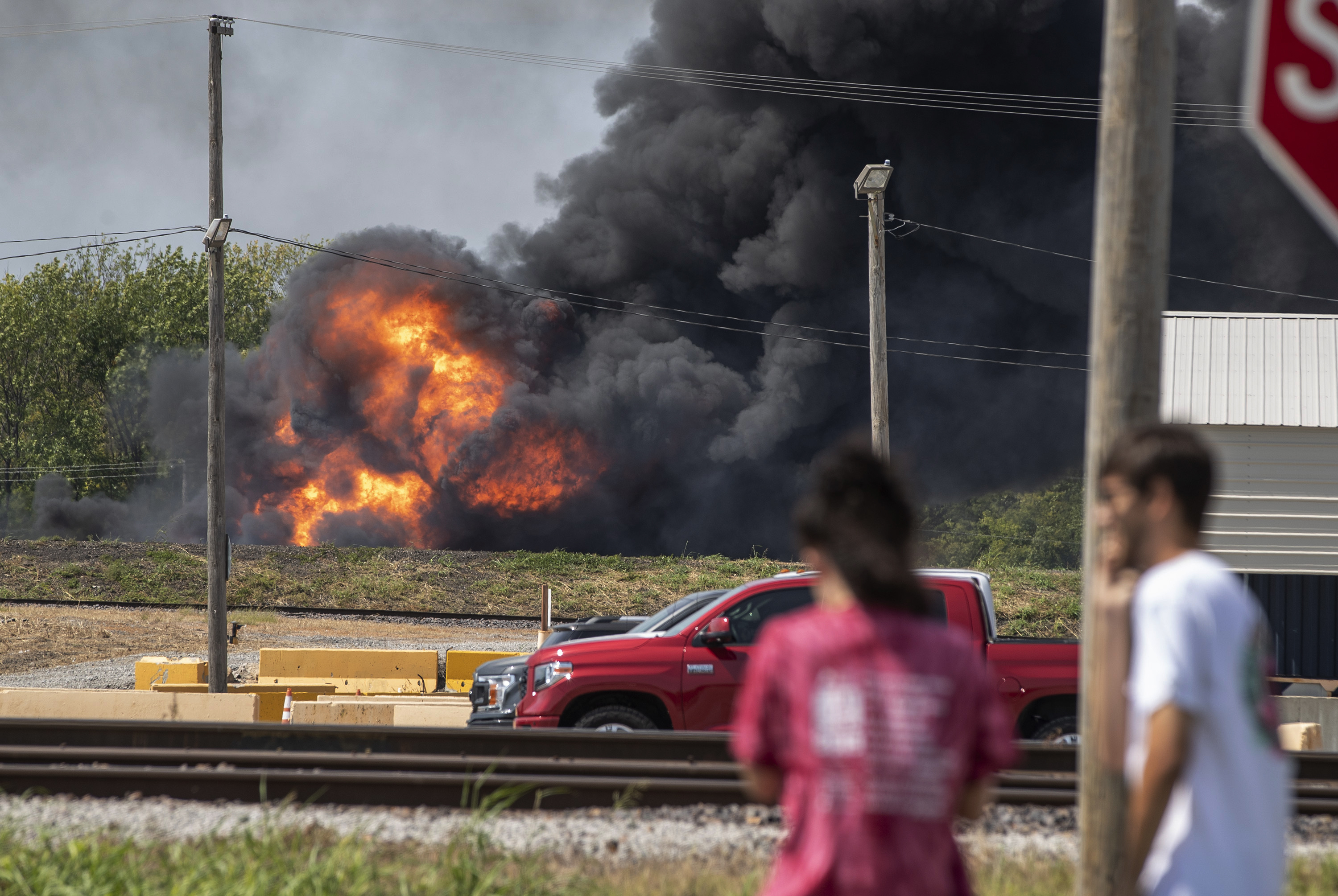 Onlookers stop in a parking lot across from a fire in the Dupo, Ill., train yard, Tuesday, Sept. 10, 2019. The freight train bearing a flammable liquid used in solvents derailed in the Illinois suburb of St. Louis Tuesday, causing the fire that sent thick, black smoke into the air and prompted the evacuation of nearby schools and residences. (Derik Holtmann / Belleville News-Democrat via AP)