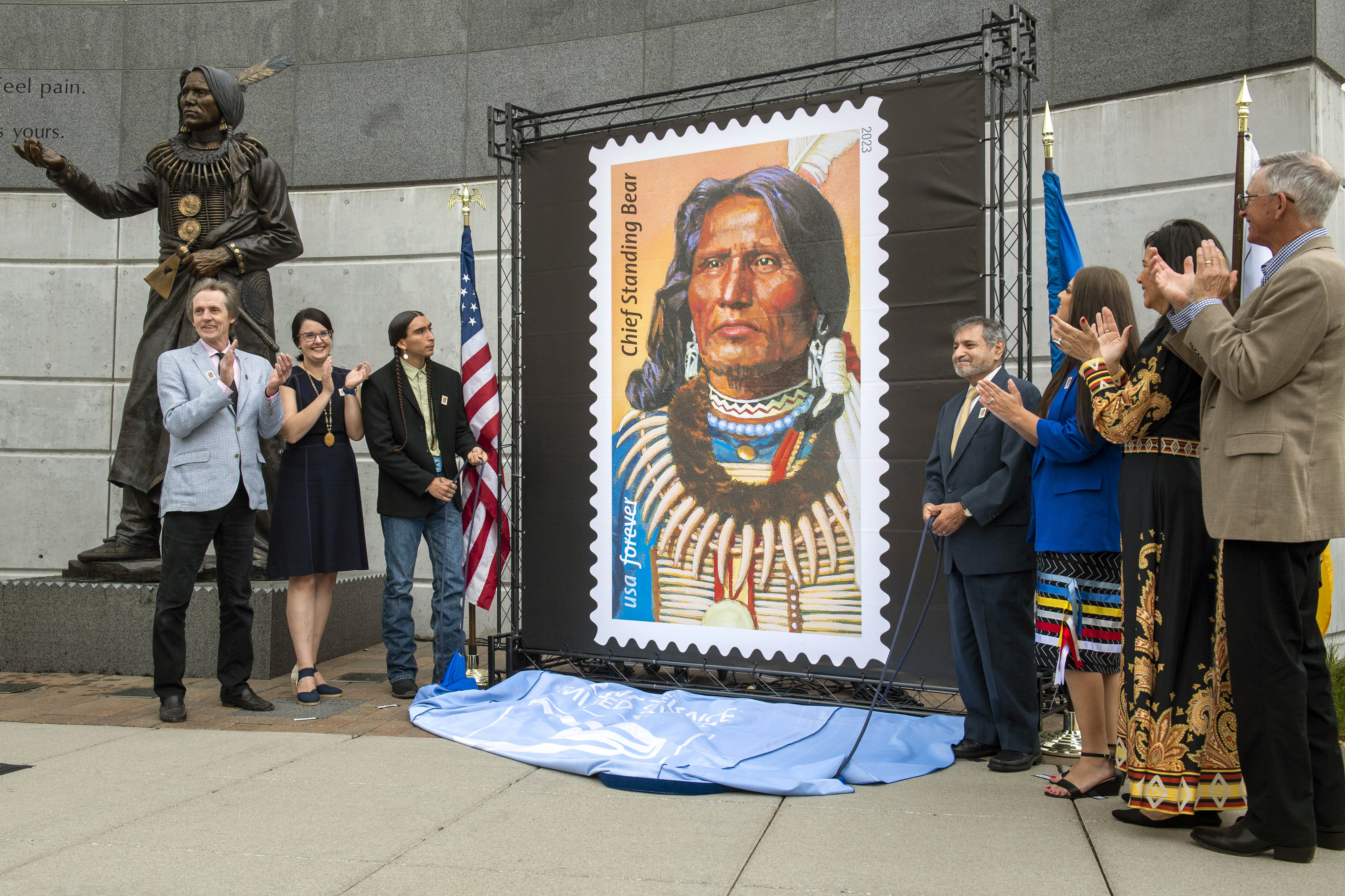 The Chief Standing Bear stamp is being unveiled by attendees from left, UNL journalism professor Joe Starita, Lincoln Parks and Recreation director Maggie Stuckey-Ross, Steve Laravie Jr., a descendant of Standing Bear, USPS Board of Governors vice chairman Anton Hajjar, Ponca tribal chairwoman Candace Schmidt, Nebraska Indian Affairs executive director Judi M. gaiashkibos, Friday, May 12, 2023, in Lincoln, Neb. Art director Derry Noyes designed the stamp.<br />(Justin Wan / Lincoln Journal Star via AP)