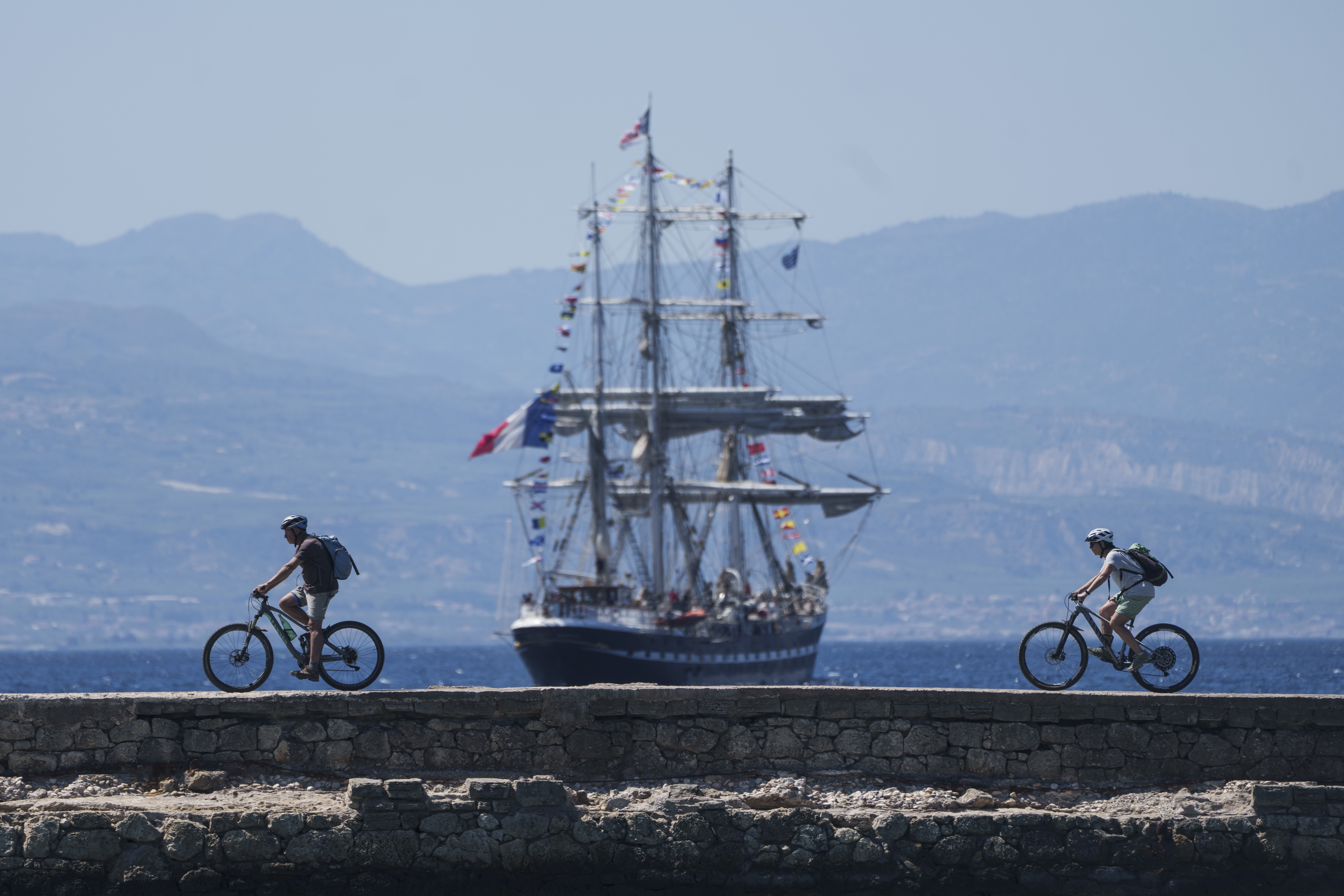 Cyclists pass in front of the Belem, the three-masted sailing ship carrying the Olympic flame to France, as it sails near Corinth, Greece, April 28, 2024.<br />(Petros Giannakouris / AP Photo)