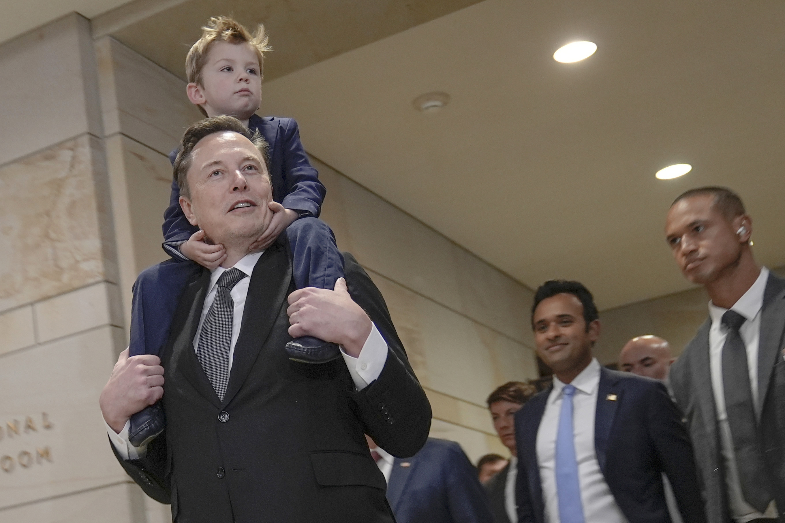 Elon Musk carrying his son X Æ A-Xii, and Vivek Ramaswamy arrive for a roundtable meeting to discuss President-elect Donald Trump&#039;s planned Department of Government Efficiency, Thursday, Dec. 5, 2024, on Capitol Hill in Washington.<br />(Mariam Zuhaib / AP Photo)