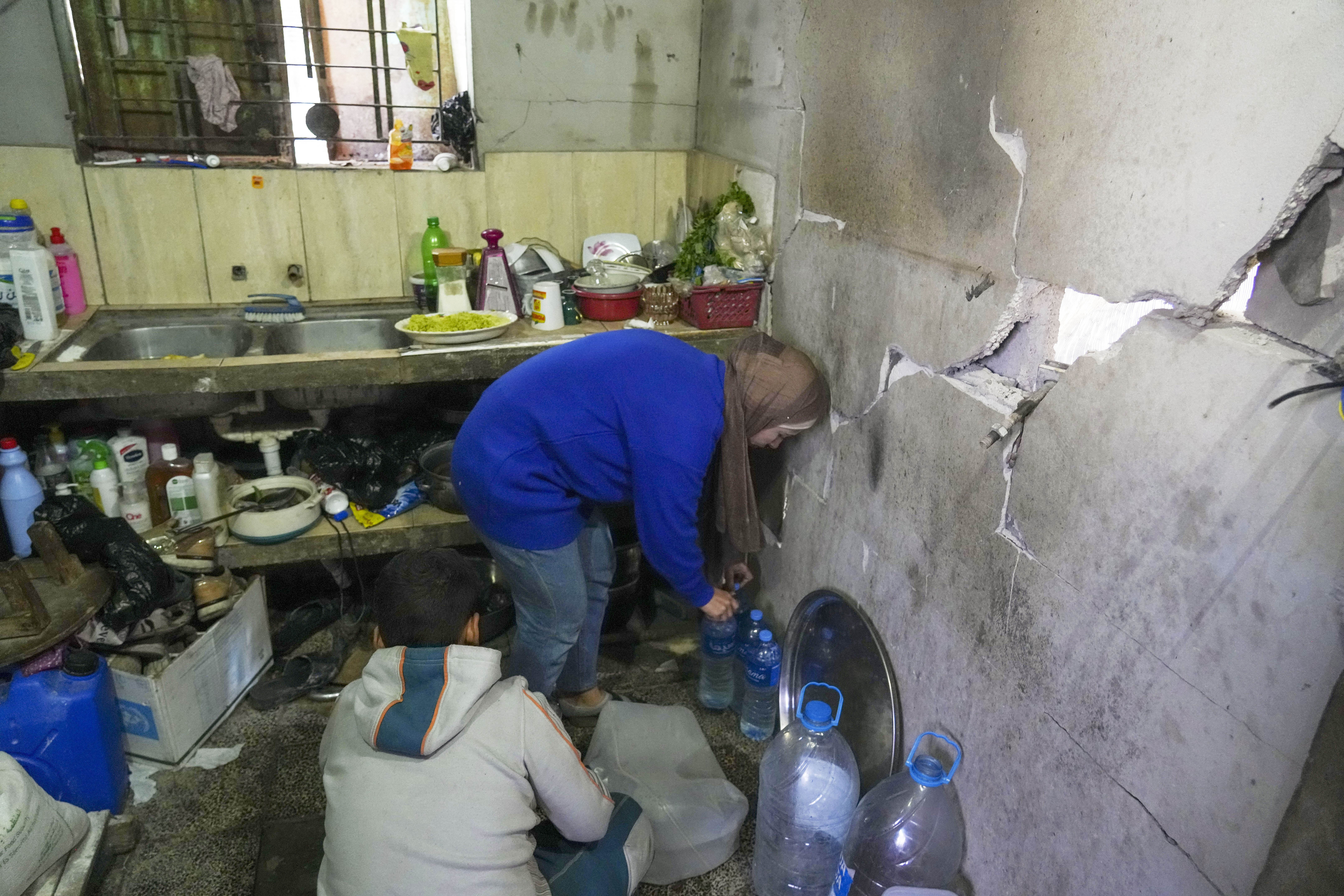 Rawia Tambora and her son Yazan fill bottles with water inside their home, which was struck by an Israeli airstrike on Oct. 20, 2023, in Beit Lahiya, northern Gaza Strip, Friday, Feb. 21, 2025.<br />(Abdel Kareem Hana / AP Photo)