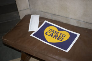 People attending a Capitol Rotunda rally left a sign on a bench in the statehouse saying, “Time to Care!” Mar. 6, 2025.<br /> (Juan Salinas II / Nebraska Examiner)