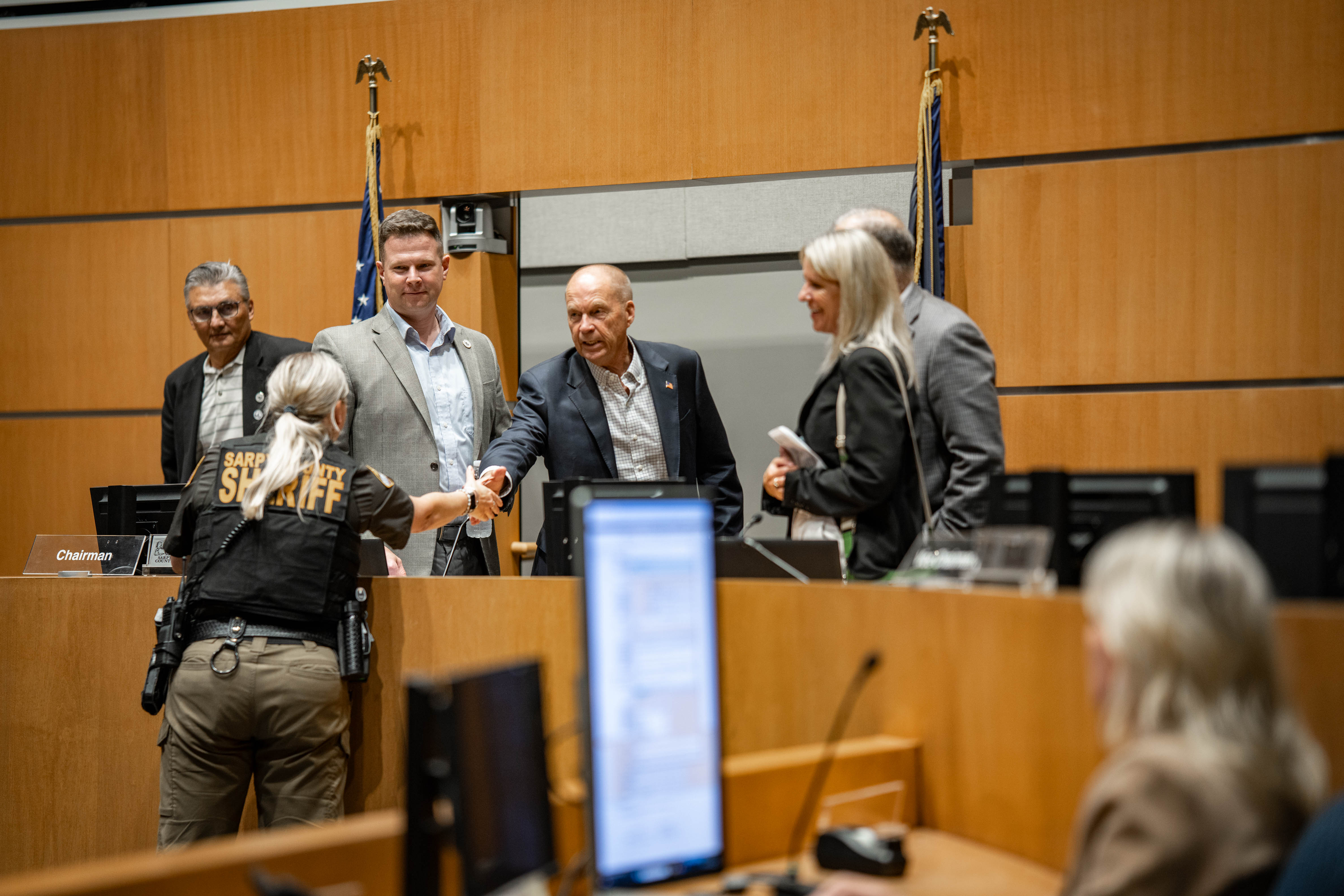 The five members of the Sarpy County Board of Commissioners shake hands with a member of the county sheriff’s department at a board meeting on June 24. From left to right: Gary Mixan, David Klug, Jim Warren, Angi Burmeister and Don Kelly.<br />(Abiolo Kosoko / Flatwater Free Press)
