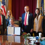 Nebraska Gov. Jim Pillen, seated (at center) holds up a newly signed executive order barring state health officials from diverting federal survivor benefits for youths in foster care to cover the costs of their care, Jan. 27, 2026.
(Courtesy of Nebraska Department of Health and Human Services)