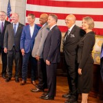 The justices of the Nebraska Supreme Court join Nebraska Gov. Jim Pillen (center left in a blue suit) and Lt. Gov. Joe Kelly (far left) for the elevation of Douglas County District Judge Derek Vaughn (center) to the Supreme Court. Vaughn’s colleagues, from left: are Justice John Freudenberg, Jason Bergevin, Jeffrey Funke (chief), William Cassel, Stephanie Stacy and Jonathan Papik, Nov. 10, 2025.
(Zach Wendling / Nebraska Examiner)