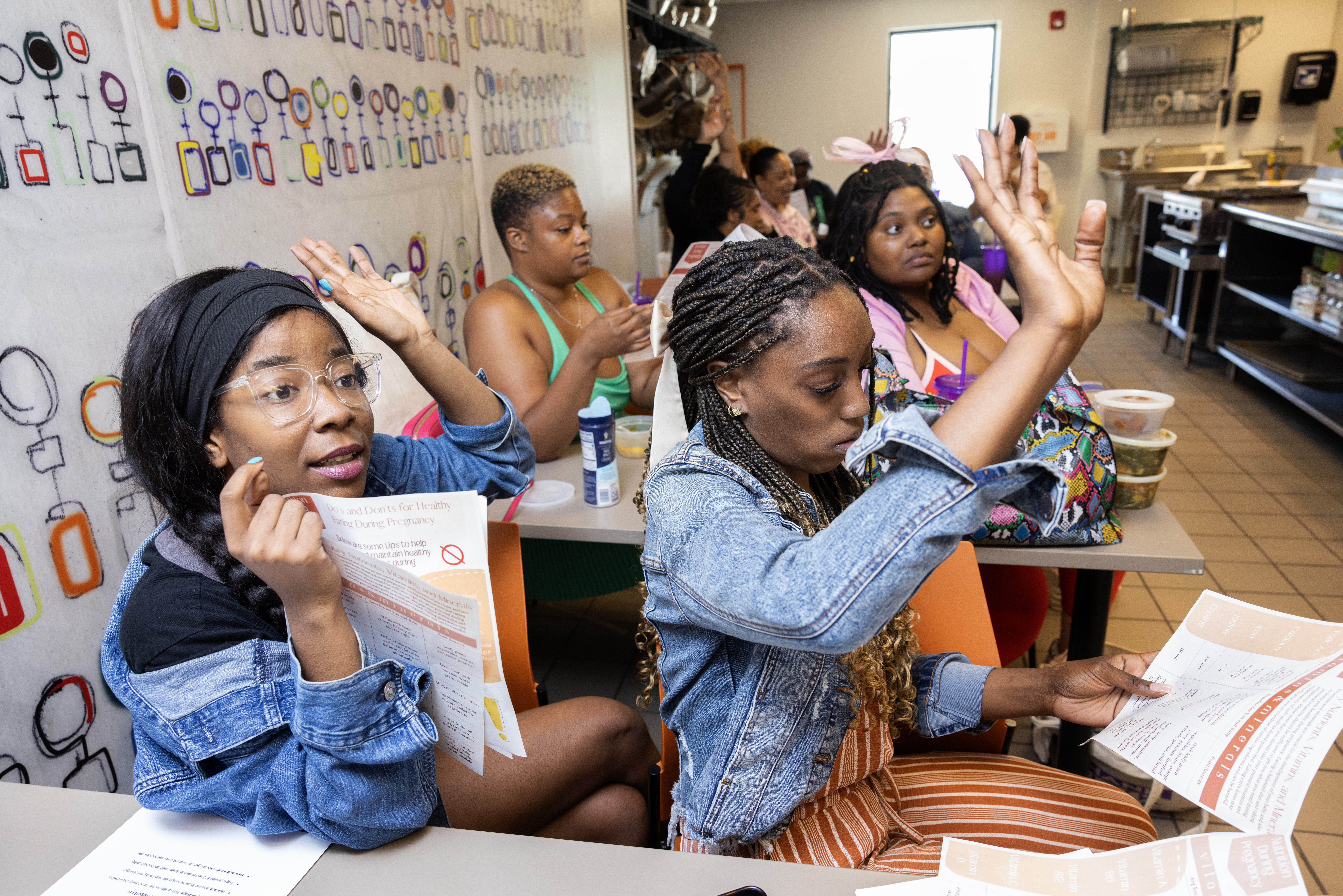 Ceteria Matthews (left) and Teyrr Bynum raise their hands during a game meant to teach about pregnancy and postpartum nutrition as part of I Be Black Girl’s Doula Passage Program.<br /> (Rebecca S. Gratz / Flatwater Free Press)