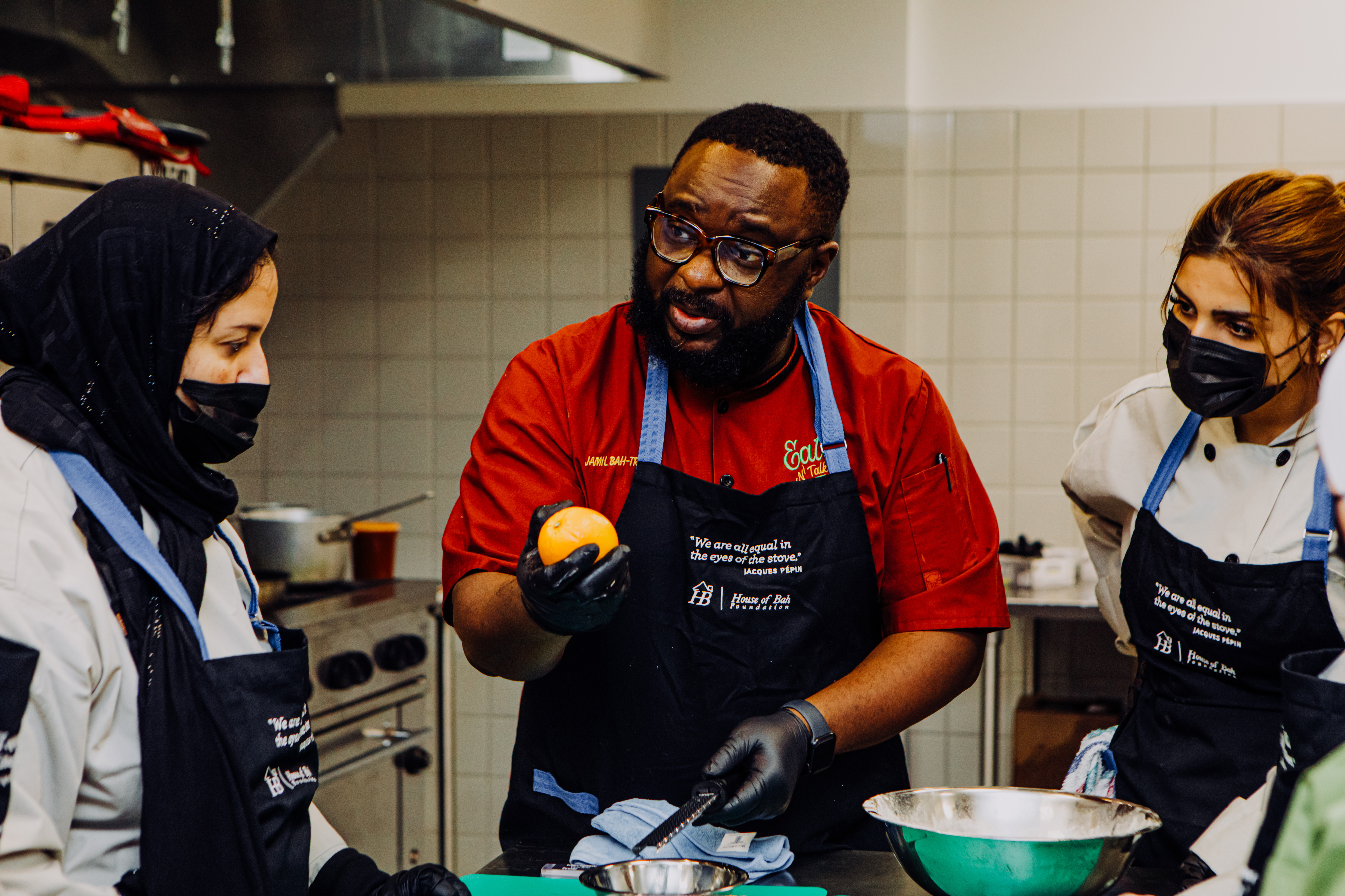 Djamil Djibril Bah-Traore (center) instructs Baaouine Naima (left) and Malalk Ashbalu (right) during a cooking class organized by House of Bah, the catering-company-turned-nonprofit that Bah-Traore started in 2015. Through classes like this one on Dec. 16, 2023, in Omaha, Bah-Traore has helped train more than 30 immigrants how to cook in a professional setting.<br />(Joshua Foo / Flatwater Free Press)
