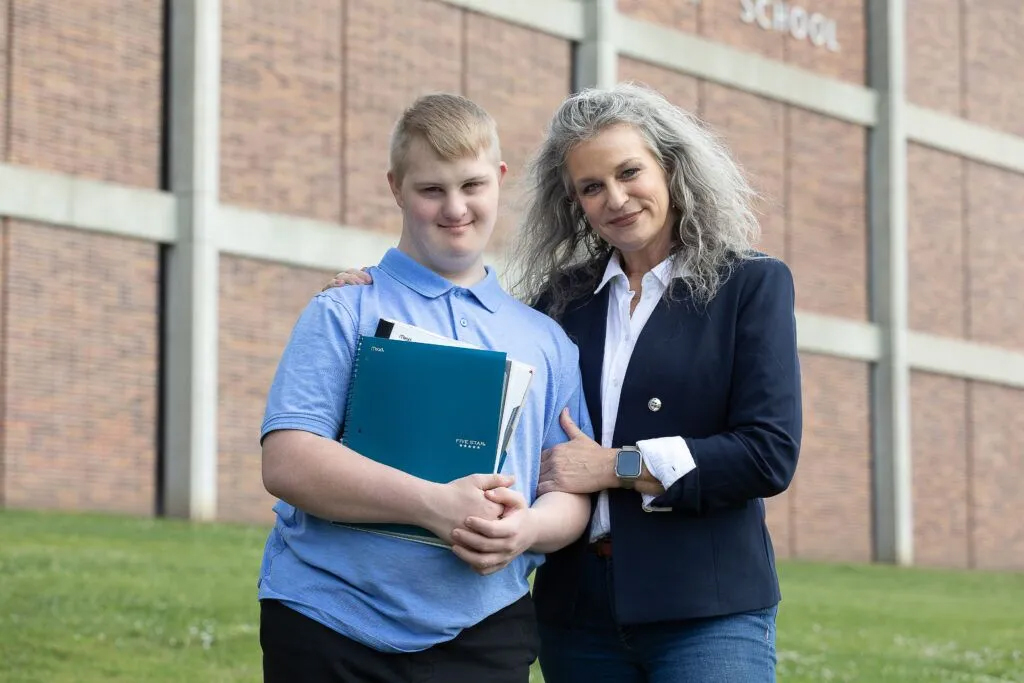 Dylan Zephier, known as “D” to his friends and family, stands with his mother Michele outside of Lincoln East High School on Thursday, May 22, 2025, the last day of classes. Dylan, who has Down syndrome and autism, will start his senior year in the fall.<br />(Liz McCue / Flatwater Free Press)