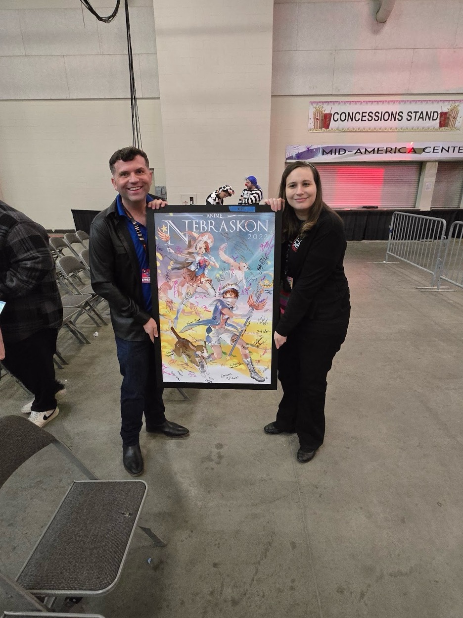 Executive Director of NAMI Nebraska, James Michael Bowers (left) holding up the highest value item sold at the NAMI Charity Auction, bought by Nebraskon Convention Chair Becky Potter (right), for $1000.<br />(Austin Petak / The Daily Record)