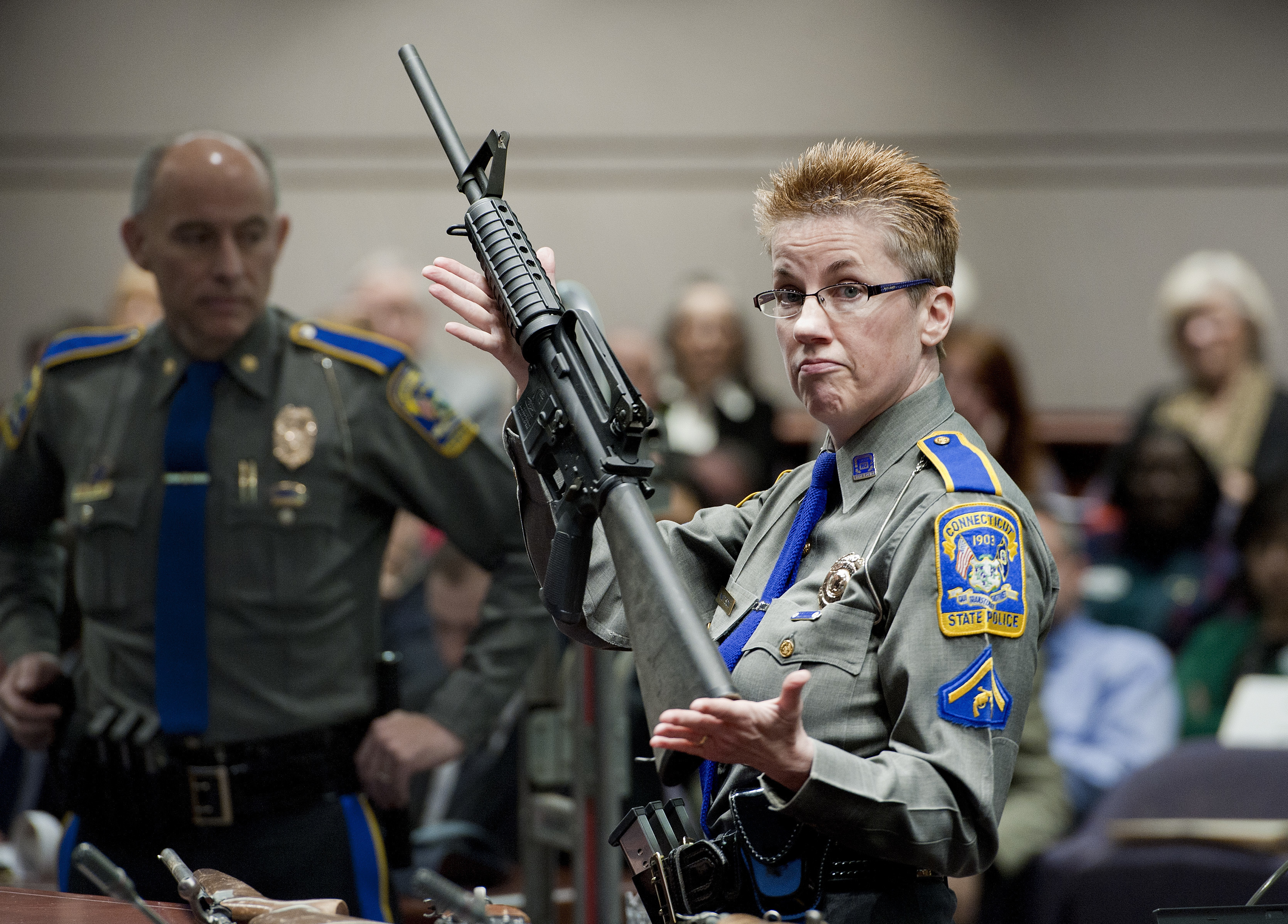 Firearms training unit Detective Barbara J. Mattson, of the Connecticut State Police, holds a Bushmaster AR-15 rifle, the same make and model used by Adam Lanza in the 2012 Sandy Hook School shooting. Neither a gun enthusiast nor a right-wing ideologue, Richard Dyke used political connections and lobster giveaways to build Bushmaster, the company that popularized assault-style rifles.<br />(Jessica Hill / AP Photo)