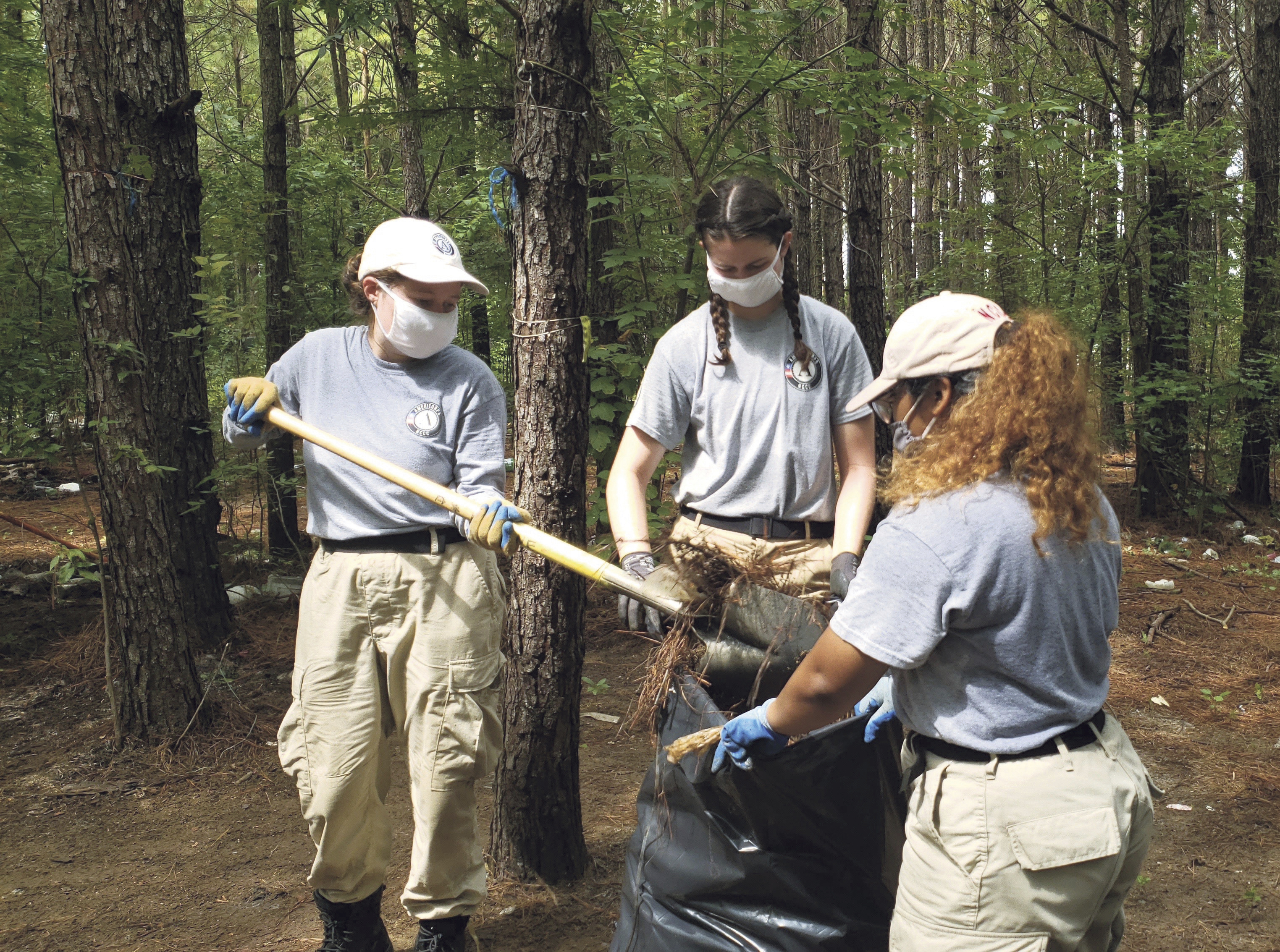 AmeriCorps members Sarah Bowman, Greta Zimmer and Rebecca Sanchez pick up trash at an abandoned homeless encampment in Meridian, Miss., on Thursday, Aug. 27, 2020.<br />(Bianca Moorman / The Meridian Star via AP)