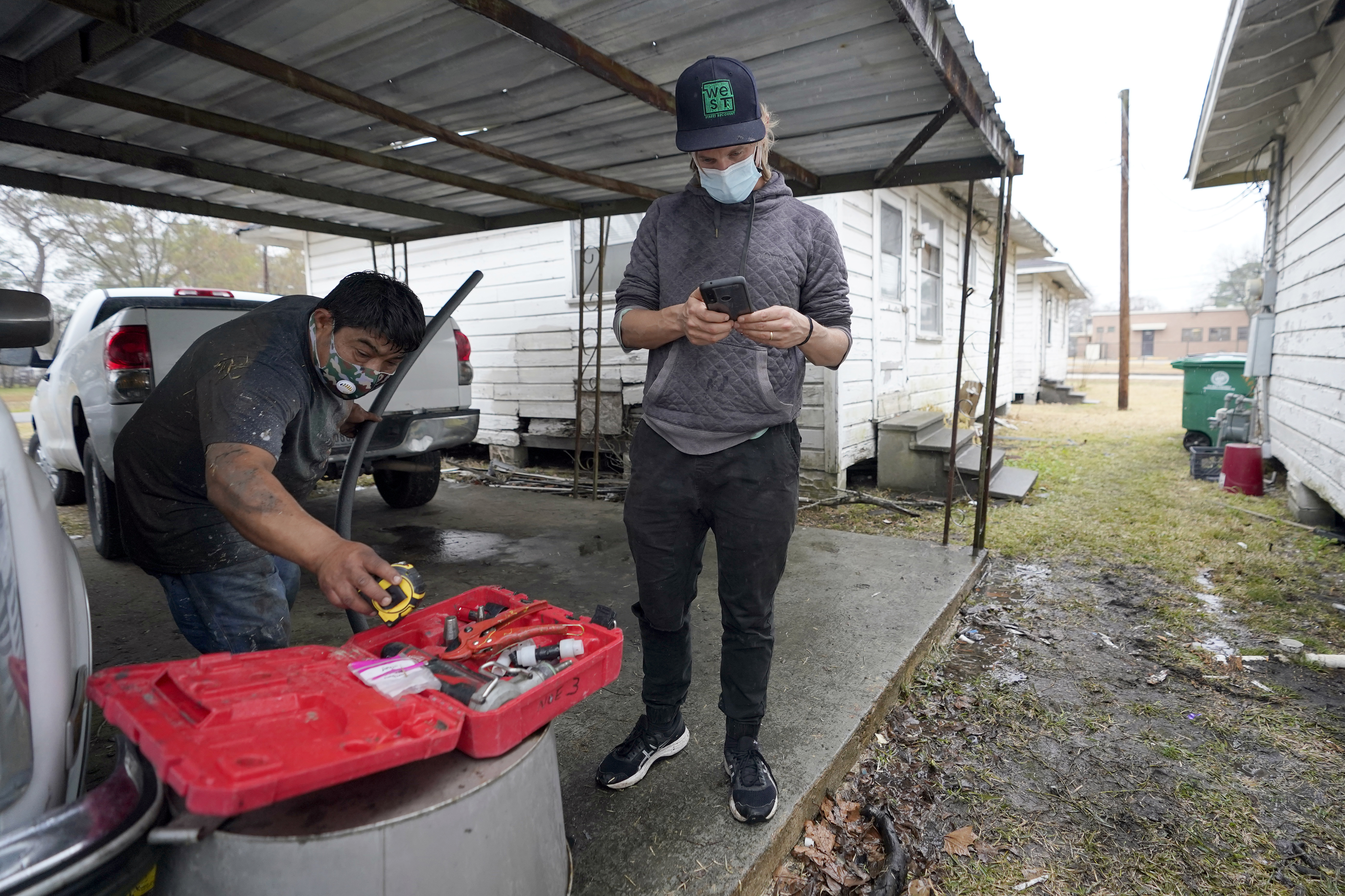 Ben Hirsch, with West Street Recovery, checks his phone as Martin Uribe reaches for tools while repairing busted pipes at a home, Thursday, Feb. 25, 2021, in Houston. West Street Recovery, a nonprofit created in the wake of Hurricane Harvey to help repair flood damaged homes, has been working since the winter storm hit to repair and replace damaged plumbing systems for residents who can&#039;t afford to do so.<br /> (David J. Phillip / AP Photo)