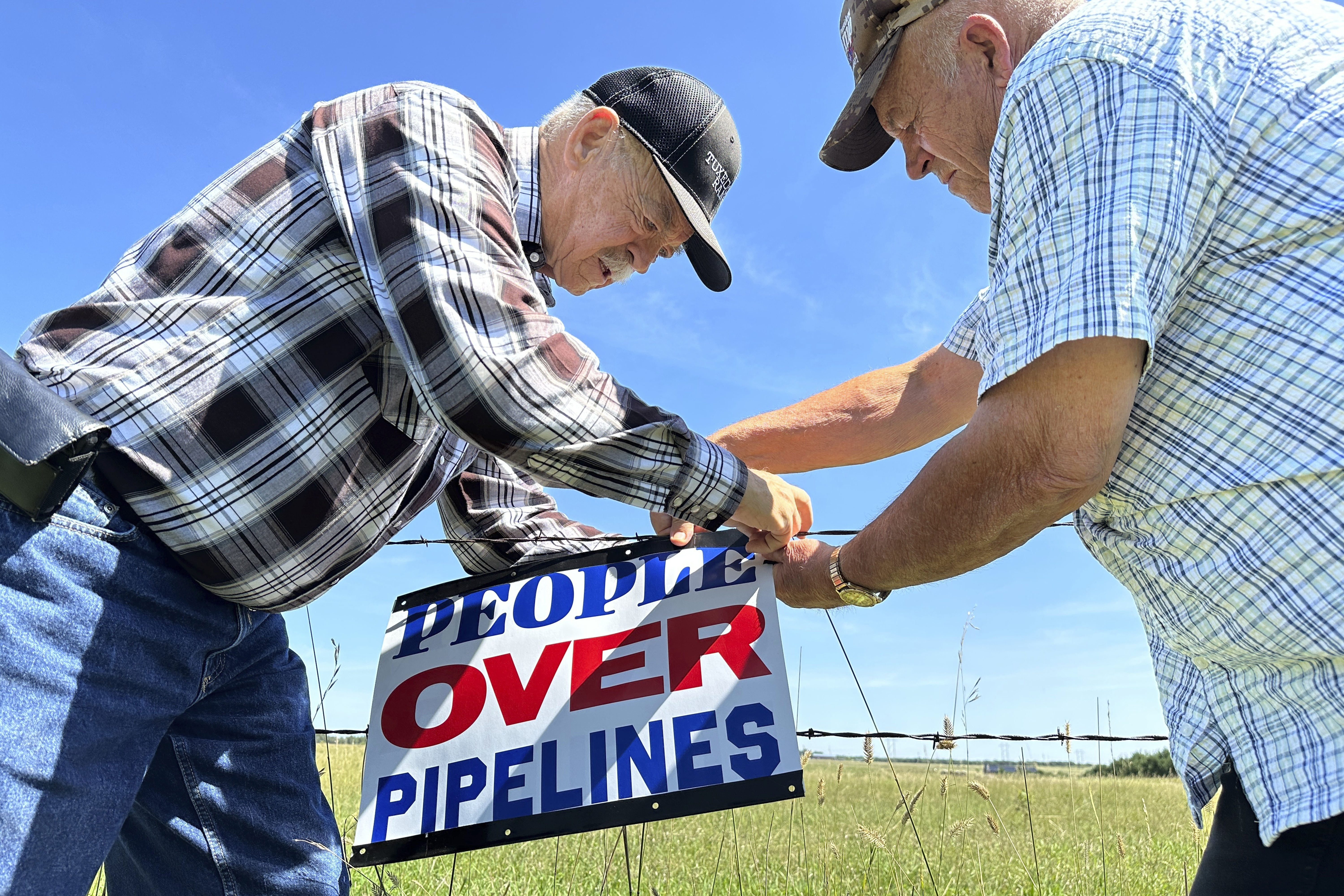Gaylen Dewing, left, and Marvin Abraham affix a sign to a roadside fence east of Bismarck, N.D., on Tuesday, Aug. 15, 2023. The sign reads “People over pipelines,” and is in opposition to Summit Carbon Solutions’ proposed five-state, 2,000-mile pipeline network to carry carbon dioxide emissions from dozens of Midwestern ethanol plants to North Dakota for permanent storage deep underground. (Jack Dura / AP Photo)