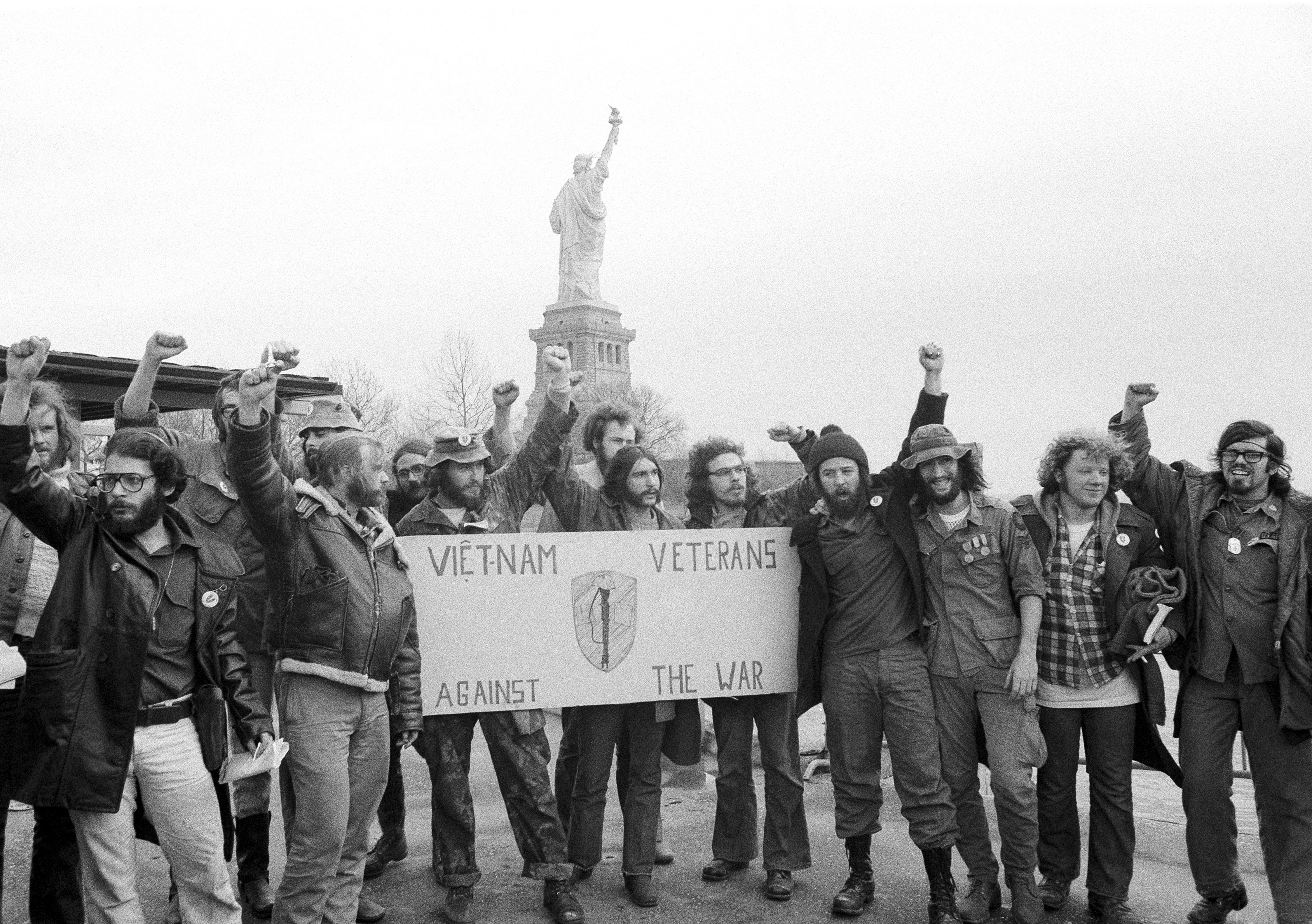 Members of the Vietnam Veterans Against the War raise clenched fists after ending their 40-hour occupation of State of Liberty, which can be seen behind them, Dec. 28, 1971. They’re hallmarks of American history: protests, rallies, sit-ins, marches, disruptions. They date from the early days of what would become the United States to the sights and sounds currently echoing across the landscapes of the nation’s colleges and universities.<br /> (Anthony Camerano / AP Photo)