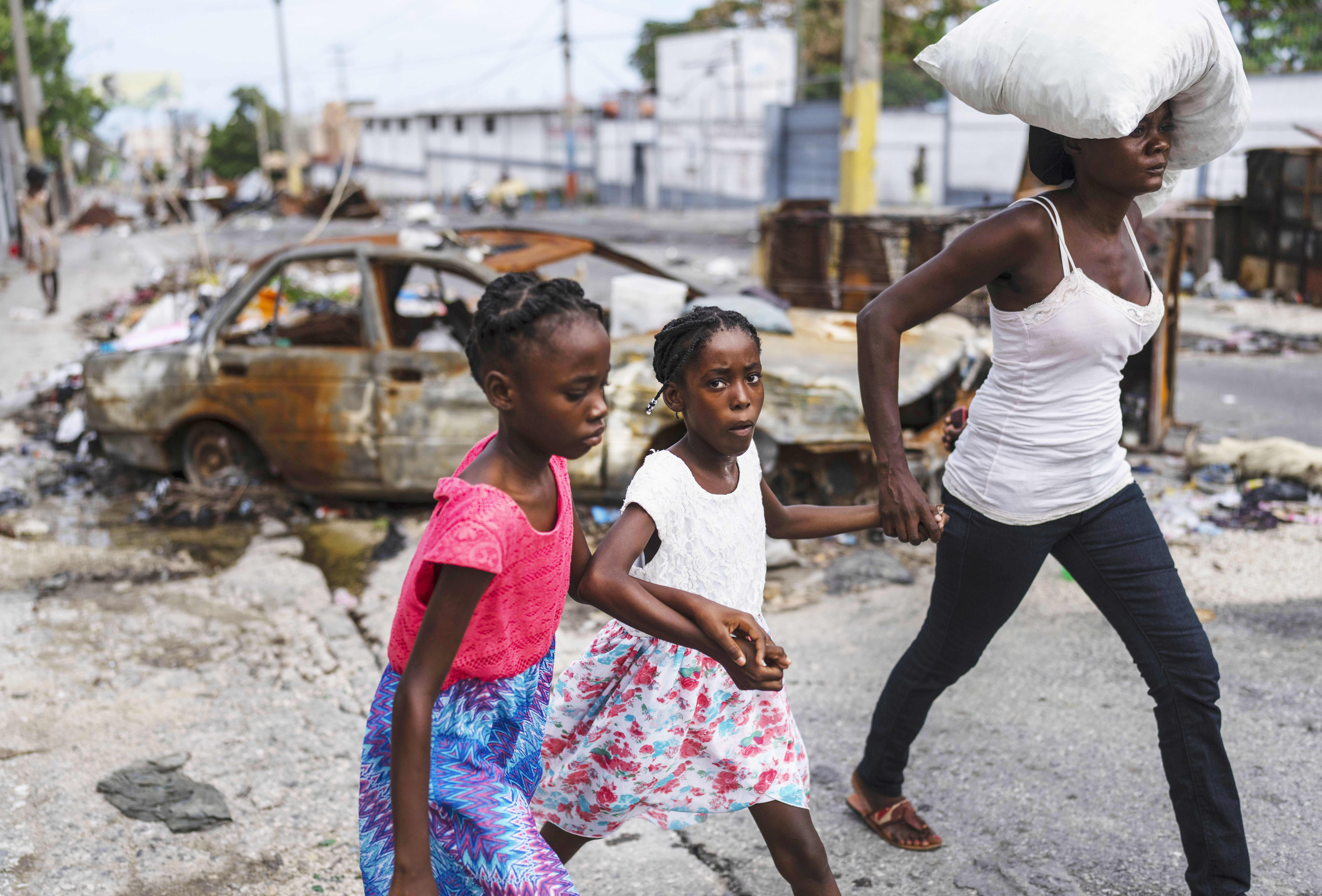 Girls holding hands are led past a burnt car blocking the street as they evacuate the Delmas 22 neighborhood to escape gang violence in Port-au-Prince, Haiti, May 2, 2024.<br />(Ramon Espinosa / AP Photo)