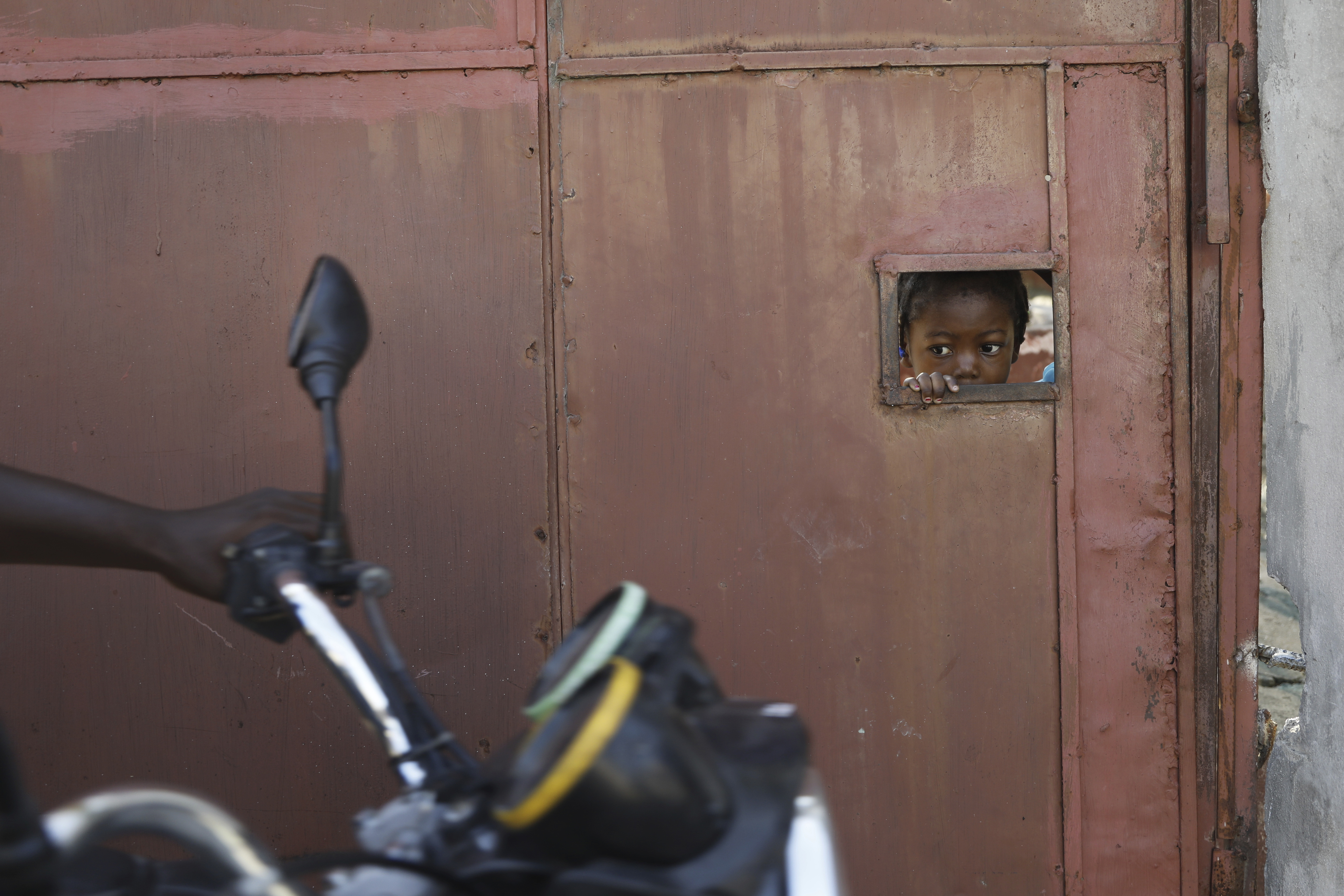 A child peers from behind a residence&#039;s security gate as she watches people flee their homes due to gang violence in Port-au-Prince, Haiti, March 9, 2024. As young Haitians are increasingly exposed to violence, the country is undergoing a wider push to dispel a long-standing taboo on seeking therapy and talking about mental health.<br />(Odelyn Joseph / AP Photo)