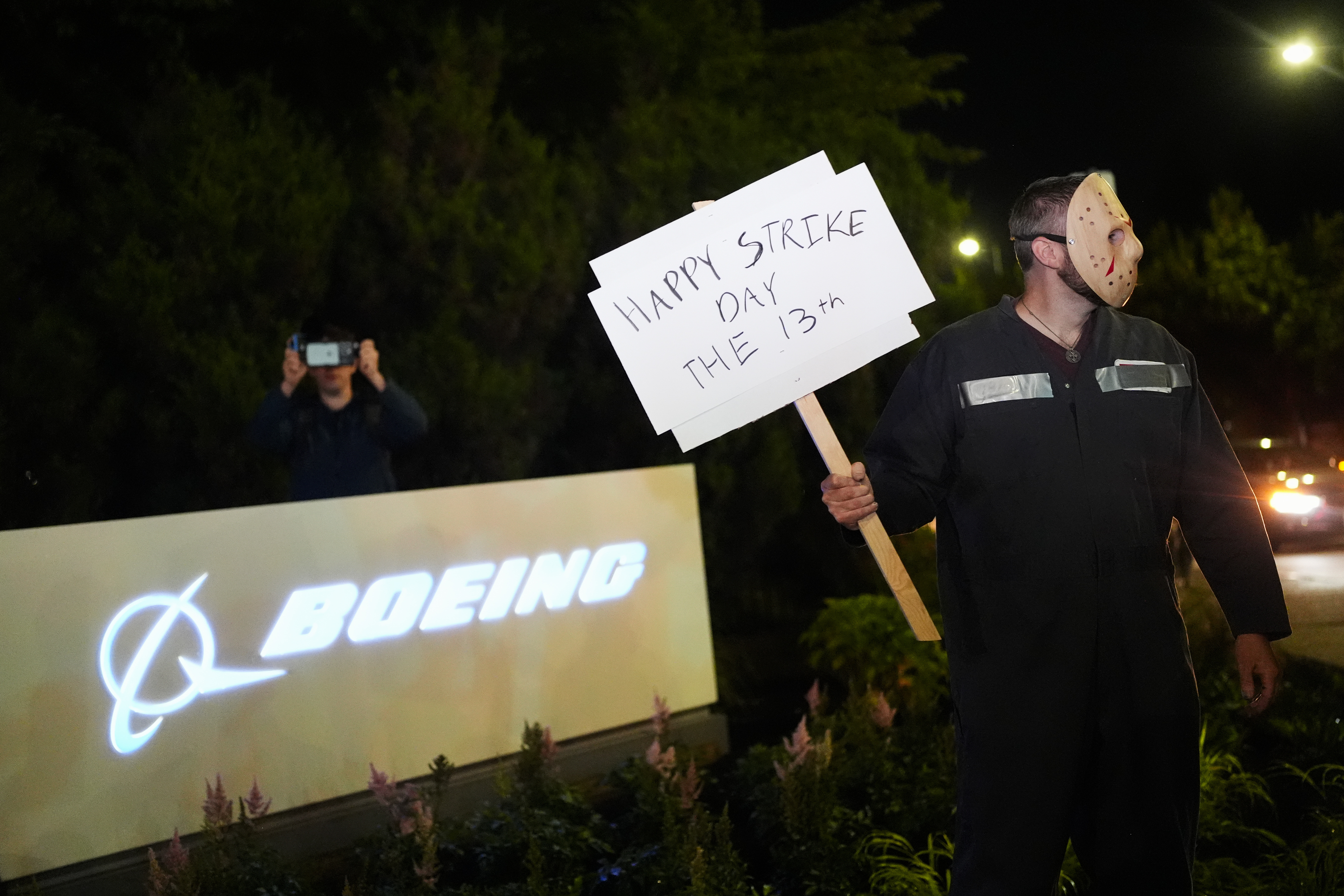 A Boeing worker wears a mask while holding a &quot;happy strike day&quot; sign after union members voted overwhelmingly to reject a contract offer and go on strike Friday, Sept. 13, 2024, outside the company&#039;s factory in Renton, Wash.<br />(Lindsey Wasson / AP Photo)
