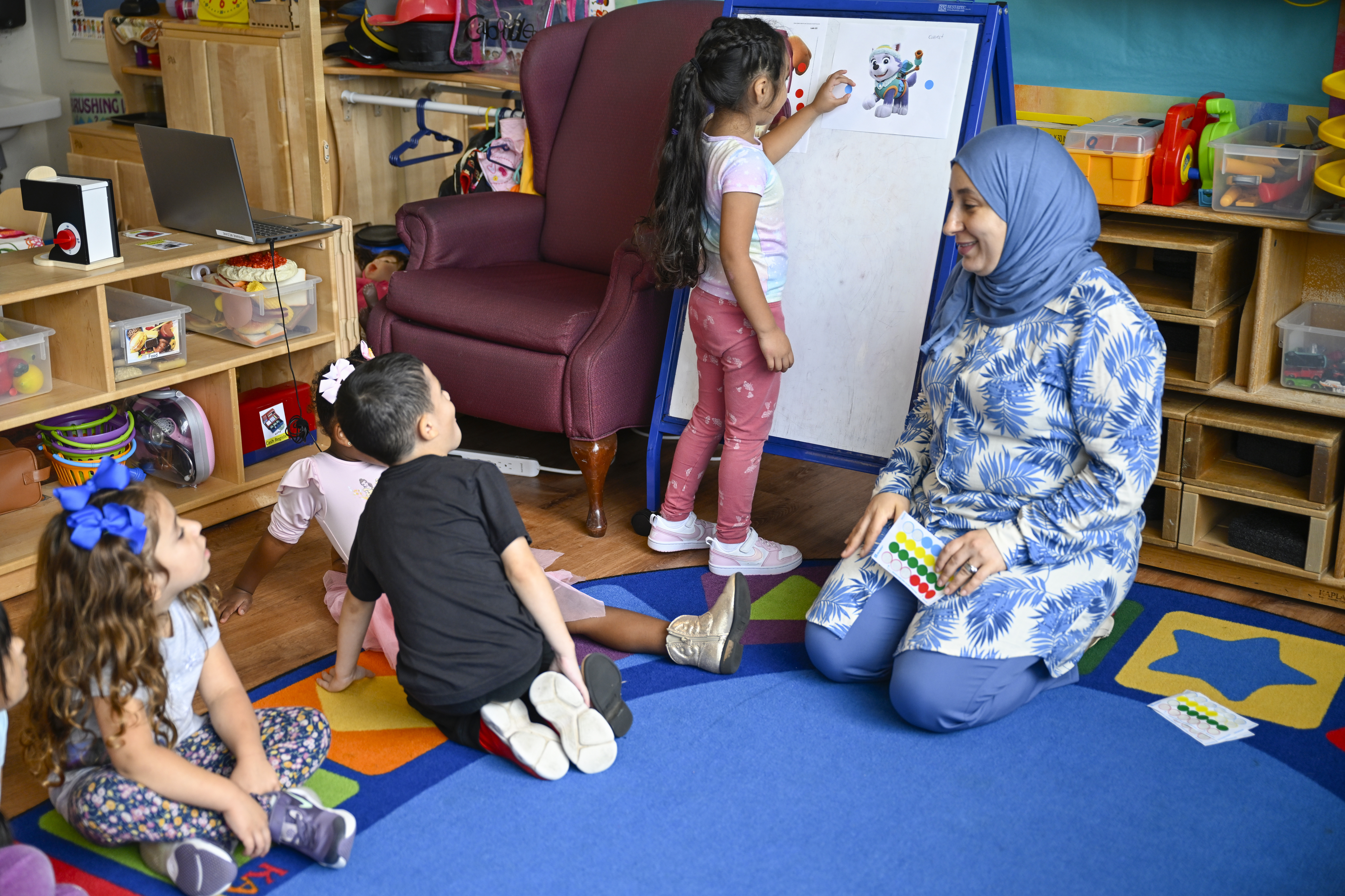 Preschool teacher Tinhinane Meziane (right) watches her students vote the most popular character of the TV show PAW Patrol at the ACCA Child Development Center, Thursday, Sept. 19, 2024, in Annandale, Va.<br /> (John McDonnell / AP Photo)