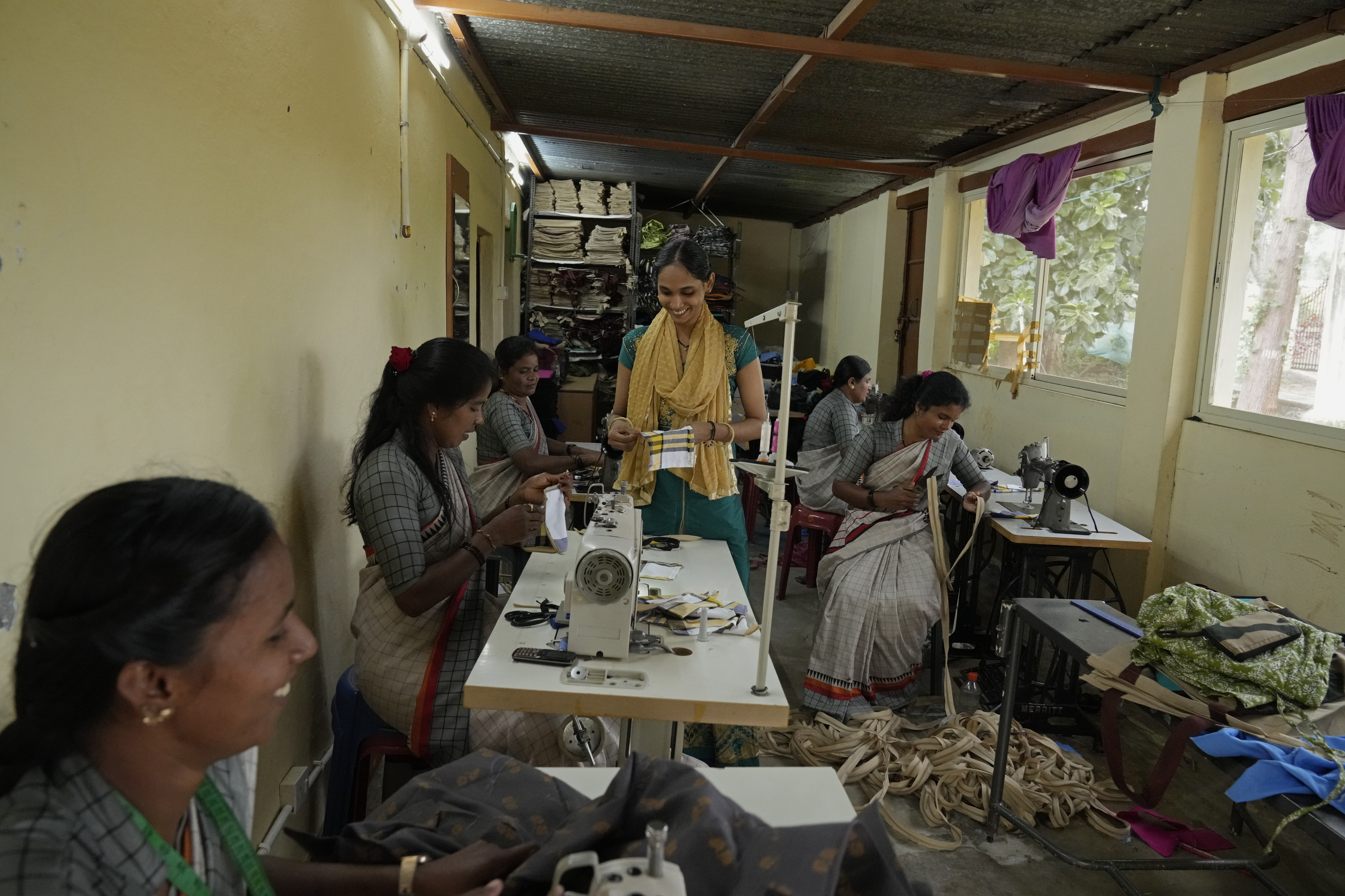A group of tailors work in a small garage using electric sewing machines to stitch office uniforms and bags at the campus of the Swami Vivekananda Youth Movement, a nongovernmental organization that works to help poor and Indigenous communities, in Kenchanahalli, India, Monday, Sept. 23, 2024.<br />(Aijaz Rahi / AP Photo)