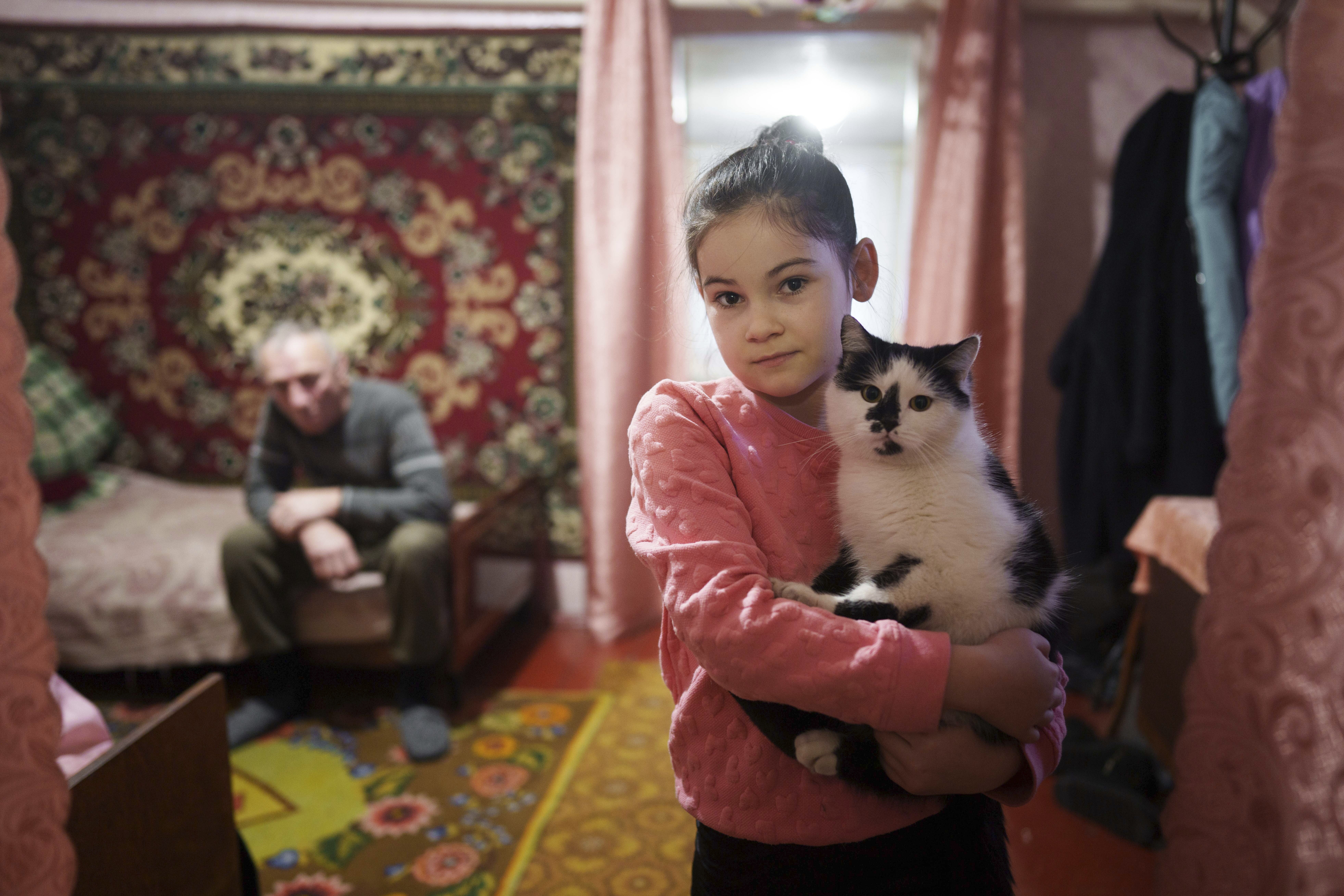 Alina Soboleva, 9, holds her cat &quot;Murchik&quot; at her house in Izium, Ukraine, Dec. 6, 2024. Her grandmother, Svitlana Lokotosh, explains that Alina has been withdrawn since witnessing the deaths of her mother and other grandmother in a shelling in the courtyard of their home.<br />(Evgeniy Maloletka / AP Photo)