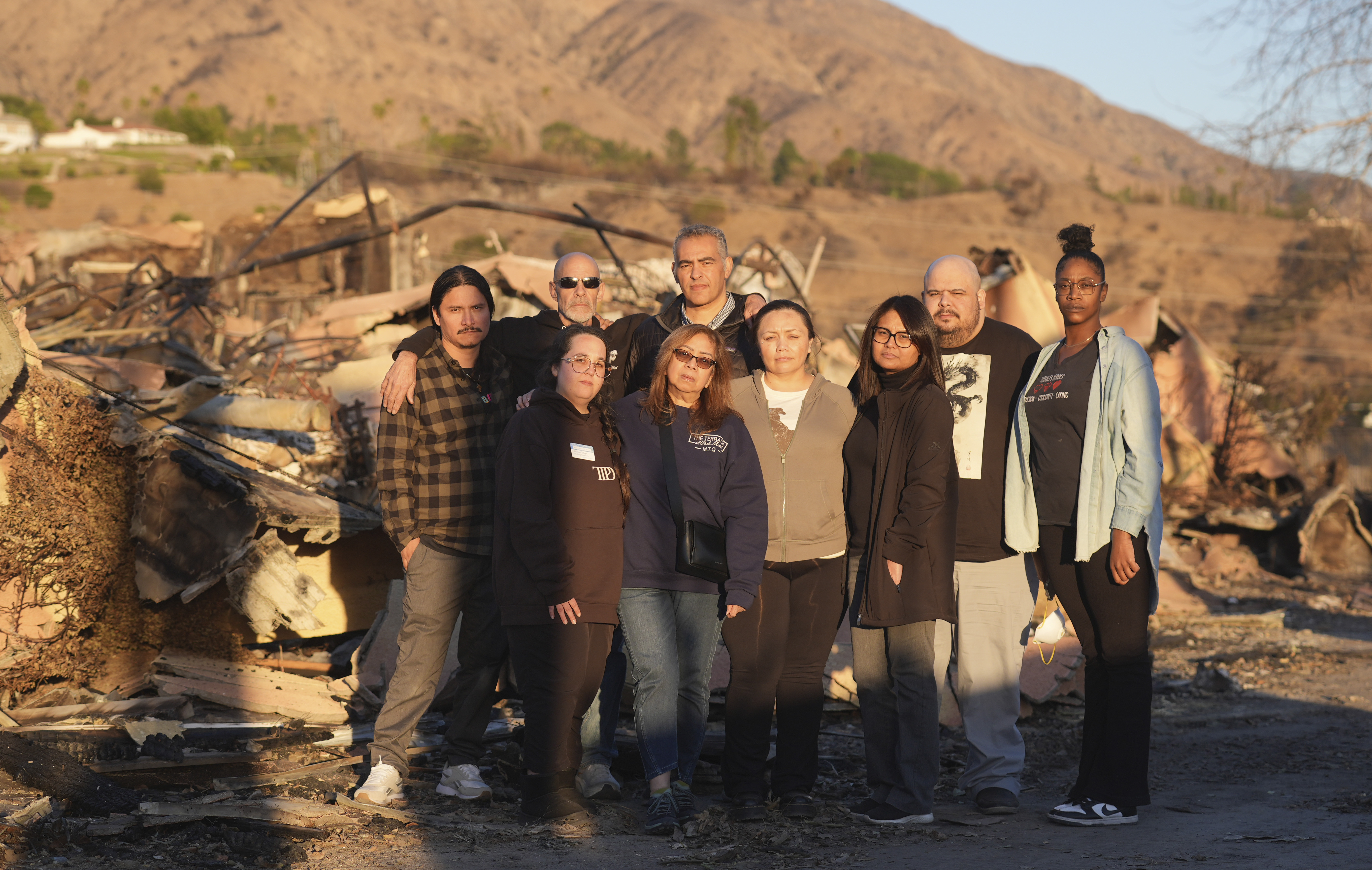Terraces at Park Marino assisted living facility staff members, back row from left: Juan Pablo Sandoval, Sam Baum and Diversified Healthcare Services President/CEO Adam Khalifa, and front row from left: Sharon Gallego, Maria Quizon, Katherine Castro, Maggie Jay, Edgardo Exia Jr. and Lashawna Thompson pose together amidst the charred remains of the facility on Monday, Jan. 13, 2025, in Pasadena, Calif.<br />(Chris Pizzello / AP Photo)