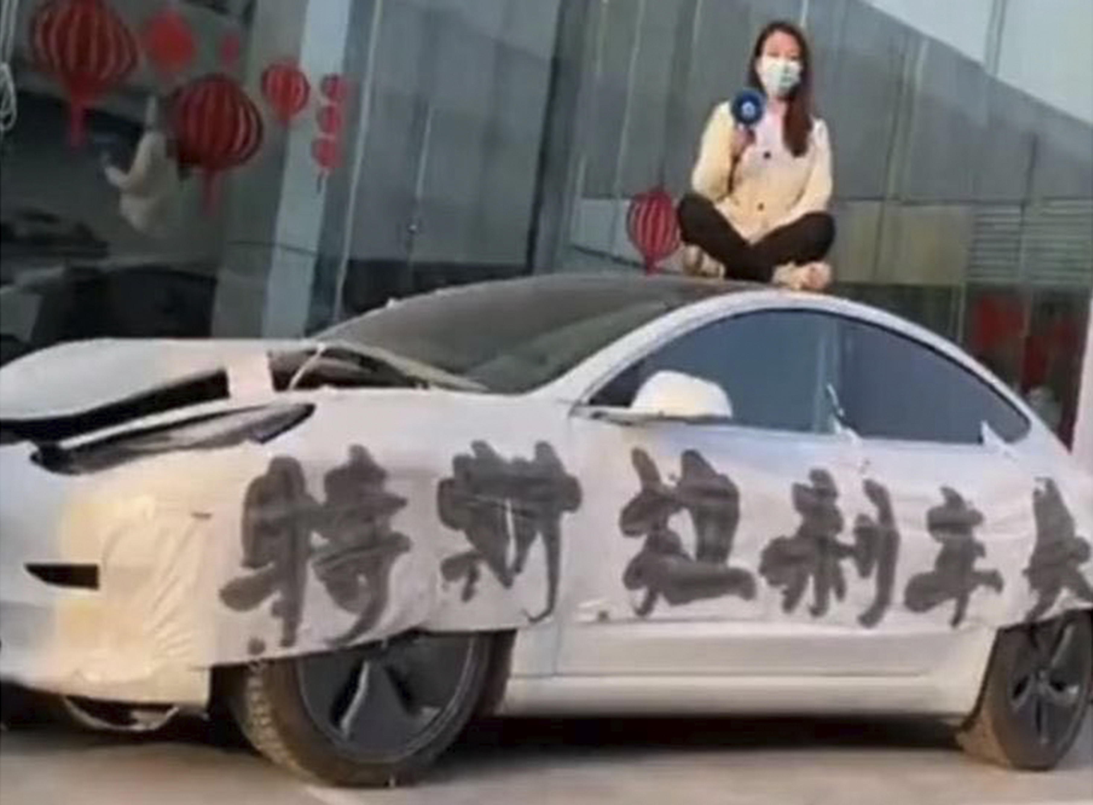 Zhang Yazhou sits on the roof of her damaged Tesla Model 3 with a bullhorn outside a Tesla dealership in Zhengzhou, the capital of central China’s Henan province, on March, 9, 2021. Banner reads, “Tesla brake failure.”<br />(Courtesy Zhang Yazhou via AP)
