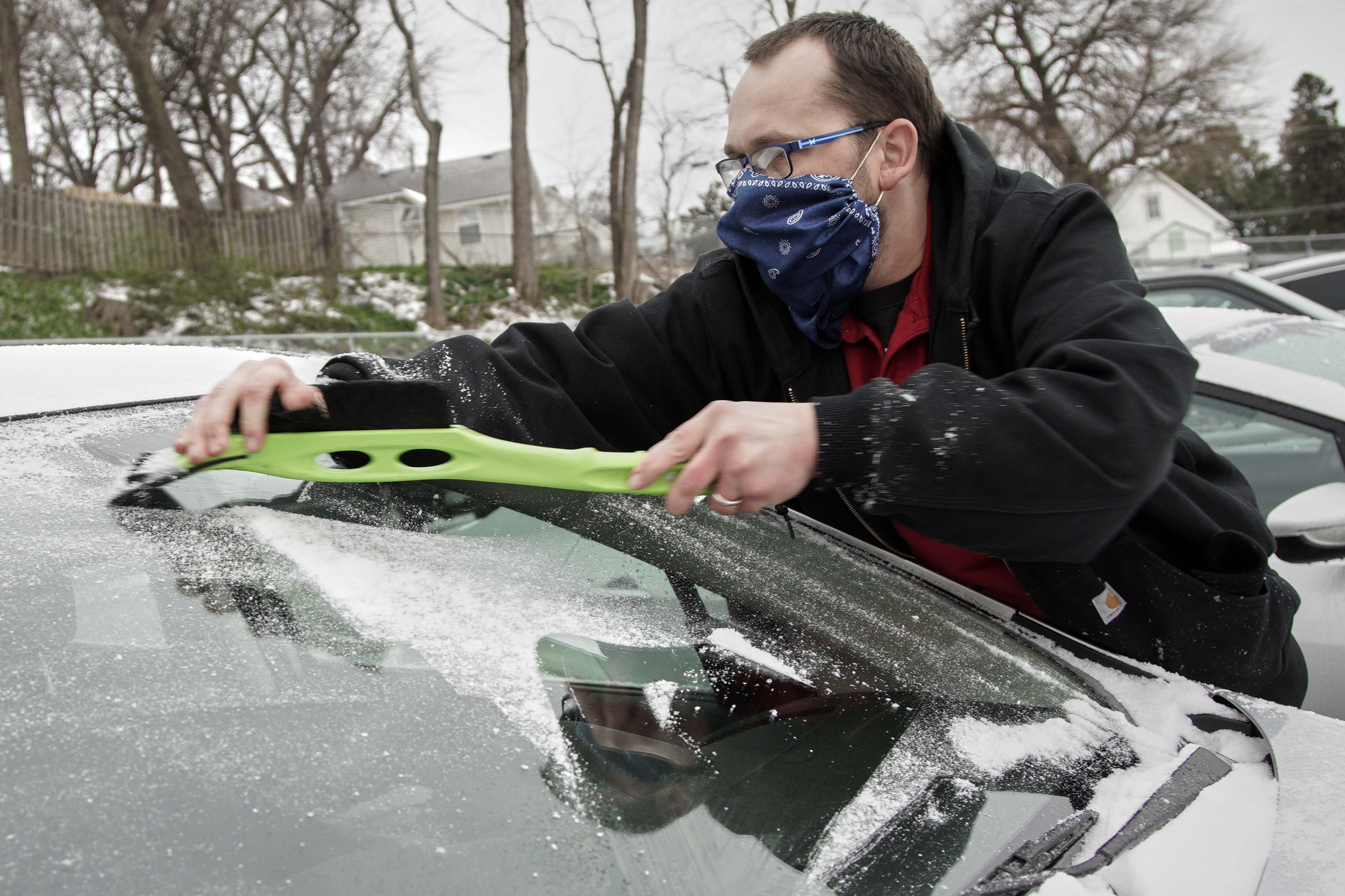 David Larrick wears a home-made mask to protect himself against the coronavirus as he clears ice and snow off of his windshield at a parking lot in Omaha, Friday, April 3, 2020. An overnight storm brought snow, freezing rain and sleet to the area. (AP Photo/Nati Harnik)