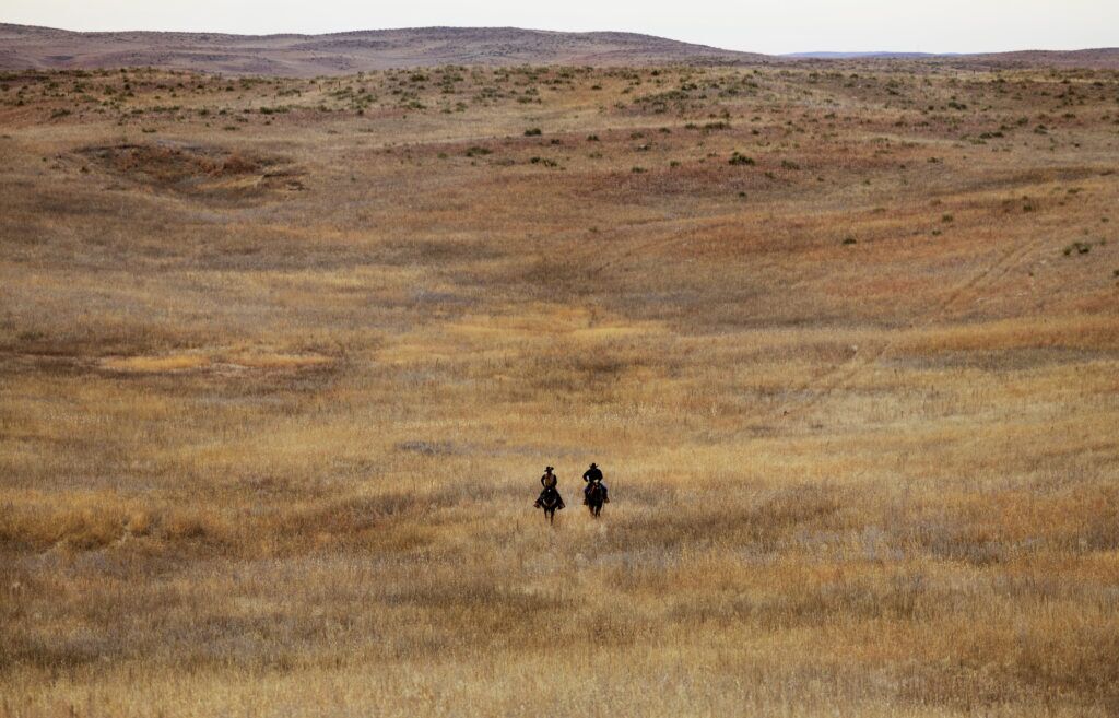 Two ranchers ride through the prairie grass on a ranch north of Keystone, Nebraska. Even with no other soul around for miles, Nebraska ranchers exist inside a globalized economy, experts say – one that will be impacted by the looming trade war.<br />(Ryan Soderlin / Flatwater Free Press)