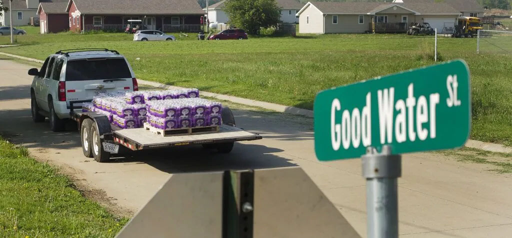 As Jessica Rouillard and Milton Denney drive about distributing bottled water, they pass by a street sign titled “Good Water St.” Tap water on the reservation has been undrinkable for almost five years.<br />(Jerry L Mennenga / Flatwater Free Press)