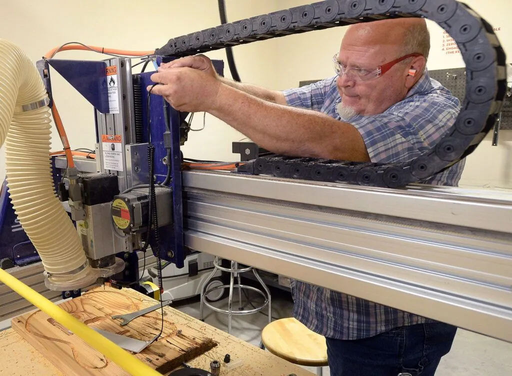 Whitmarsh makes an adjustment on a CNC milling machine as he fashions a guitar body at the Nebraska Innovation Studio in Lincoln on July 8, 2024. It was fashioned from old-growth pine originally used to build a grain elevator in Hamburg, Iowa, some 125 years ago.<br />(Eric Gregory / Flatwater Free Press)