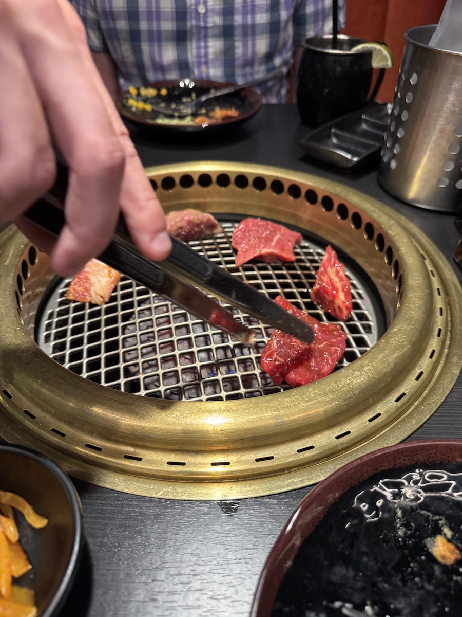A server places one piece of each meat on the platter onto the in-table grill to get the cooking started.<br />(Sarah Baker Hansen / Flatwater Free Press)