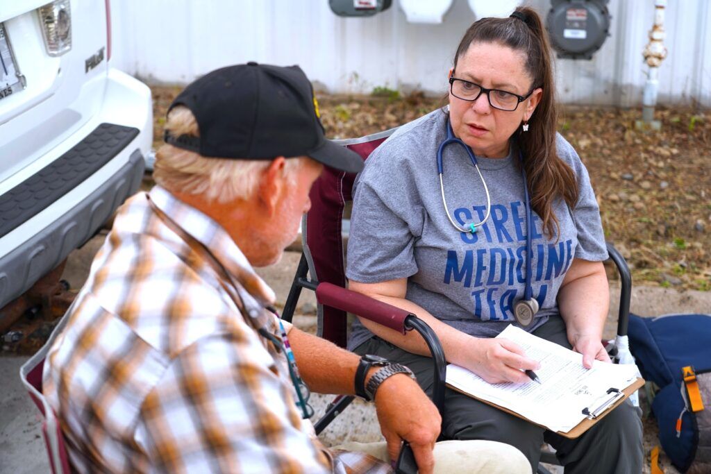 Melissa Neuenfeldt listens to Wayne Birkholtz discuss his medical needs and what medication he takes on Sept. 9, 2024. Neuenfeldt met Birkholtz outside his car where he’s currently living. As a nurse with HEAL Omaha, which provides healthcare to Omaha’s unsheltered homeless population, she hopes helping manage their health can create a clearer path toward housing stability.<br />(Chris Bowling / Flatwater Free Press)