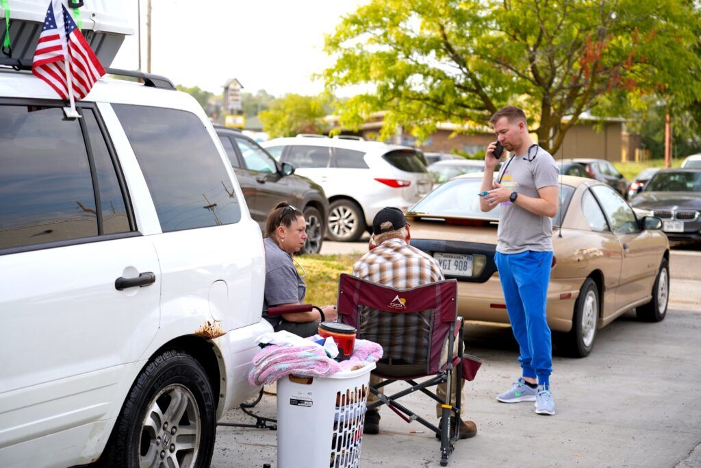 Melissa Neunfeldt (left) listens to Wayne Birkholtz (middle) while Dr. Dalton Nelsen (right) tries to set up his prepaid phone on Sept. 9, 2024. Neunfeldt and Nelsen are volunteers with HEAL Omaha which provides street medicine to Omaha’s unsheltered homeless population.<br />(Chris Bowling / Flatwater Free Press)