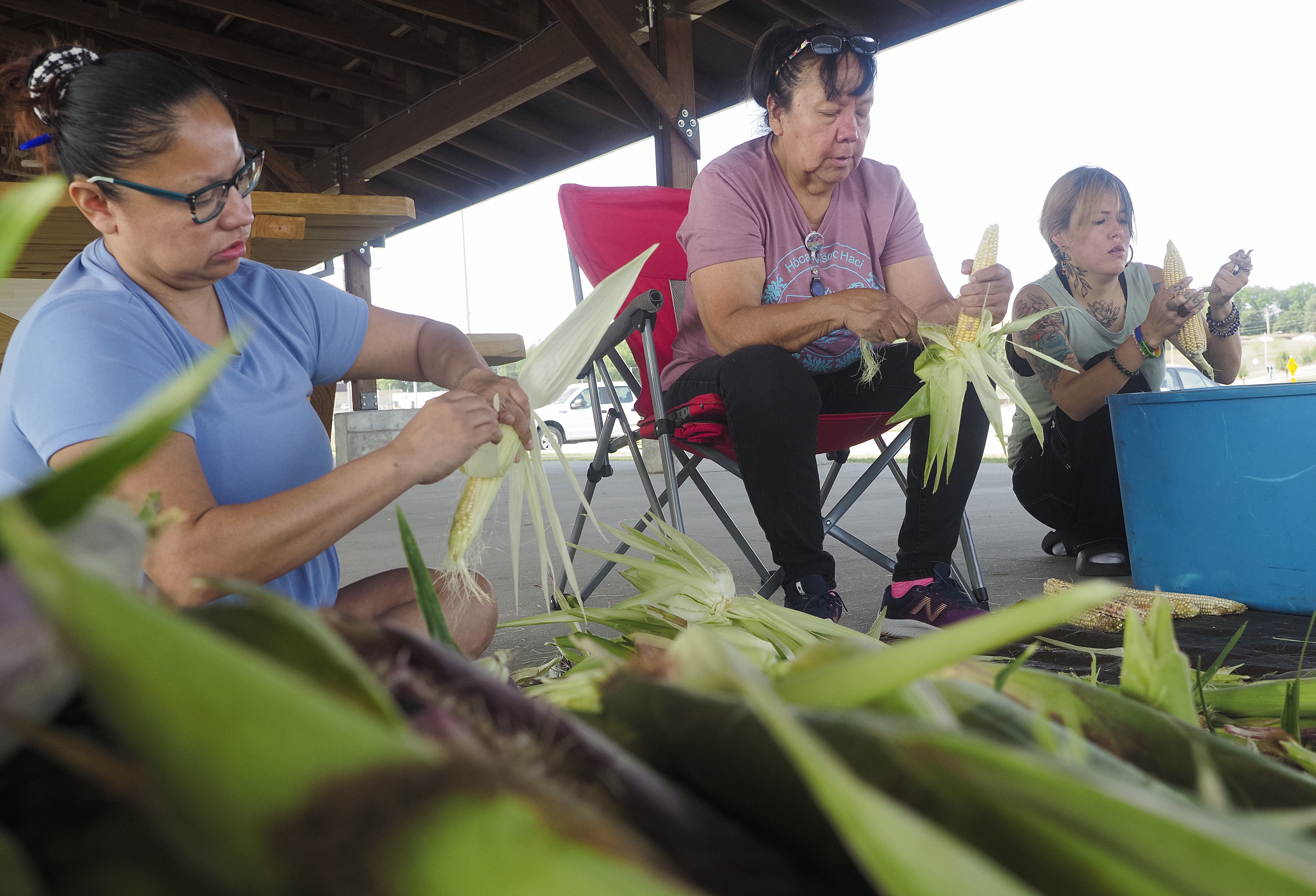Members of the Winnebago Tribe of Nebraska Candace Payer (left), Nona Bearskin and Jordana Bass husk harvested corn at the Ho Chunk Village Farmer’s Market area in Winnebago, Nebraska, Sept. 5. (Jerry L Mennenga / Flatwater Free Press)