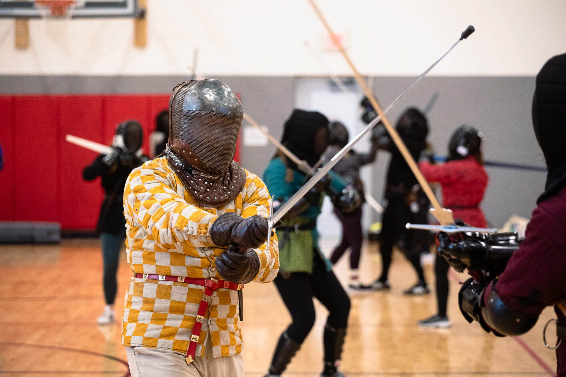 Participants at the Nebraska Swordfighters Guild’s January Fight Camp wear colorful gambesons – traditional padded or quilted jackets that would have been worn under armor in medieval combat. The gambesons, along with gloves, gorgets (steel or leather garments that protect the neck) and masks help fighters stay safe during exercises and sparring.<br />(Liz McCue / Flatwater Free Press)