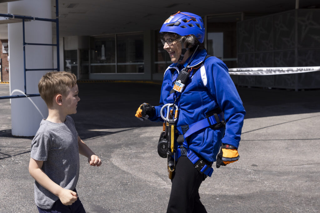 Sister Stephanie Matcha dances with her great-nephew, Walter Hill, 6, after she rappelled down the side of The Highline Apartments in downtown Omaha on May 3, 2025. Matcha had a large cheering section among Siena Francis staff and volunteers at the event, a fundraiser for the Siena Francis House.<br />(Anna Reed / Flatwater Free Press)