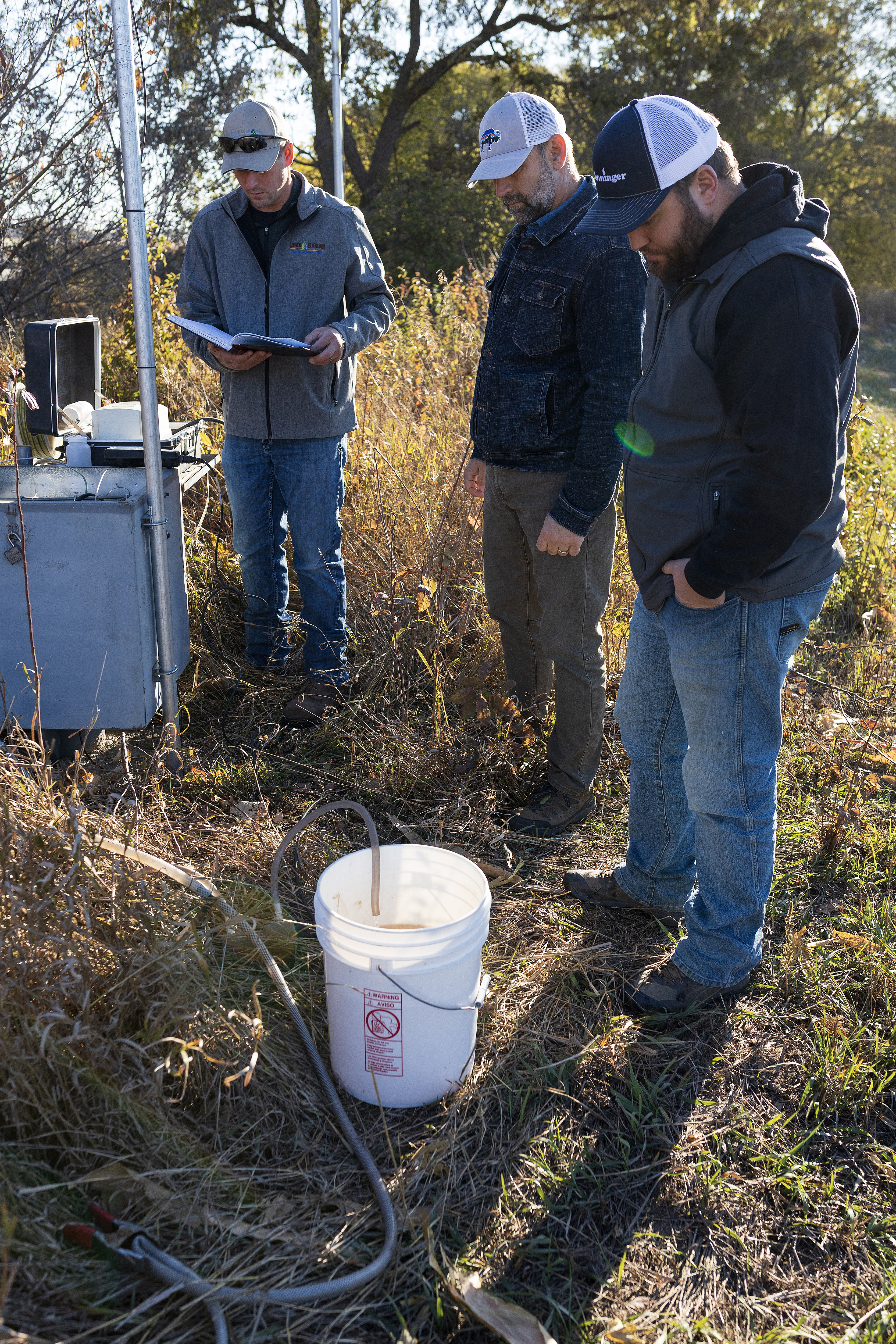 Water resources technicians Josh Schnitzler, left, and Connor Baldwin, right, and assistant general manager Brian Bruckner, center, who all work for the Lower Elkhorn Resources District in Norfolk, test the water in a monitoring well near the north fork of the Elkhorn River.  (Ryan Soderlin / Flatwater Free Press)