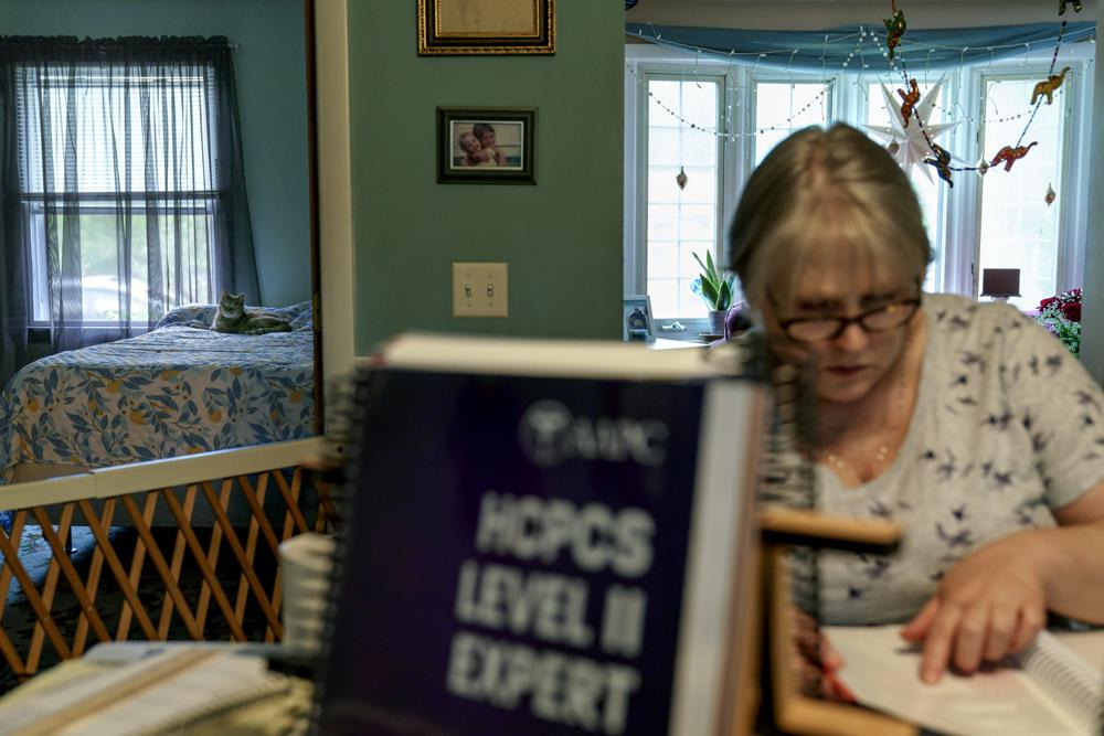 Ellen Booth, 57, studies at her kitchen table to become a certified medical coder as her cat, Juji, sits on a bed behind her in Coventry, R.I., Monday, May 17, 2021. When the restaurant she worked for closed last year, Booth said it gave her “the kick I needed.” She started a year-long class to learn to be a medical coder. (AP)