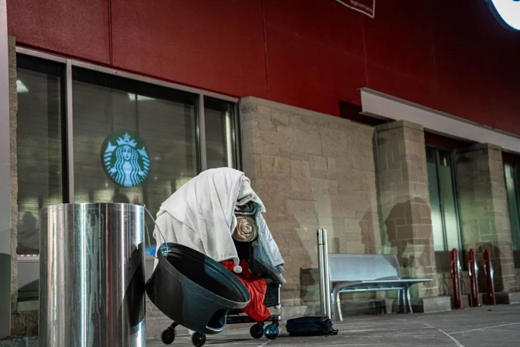 A shopping cart piled with blankets stands outside the entrance to Target on 72nd and Dodge streets on Jan. 21, 2025. Jonathan Martin covers himself with blankets to sleep outside through the winter in Omaha. A cold front brought temperatures nearing -30 degrees with wind chill the night before.<br />(Abioloa Kosoko / Flatwater Free Press)