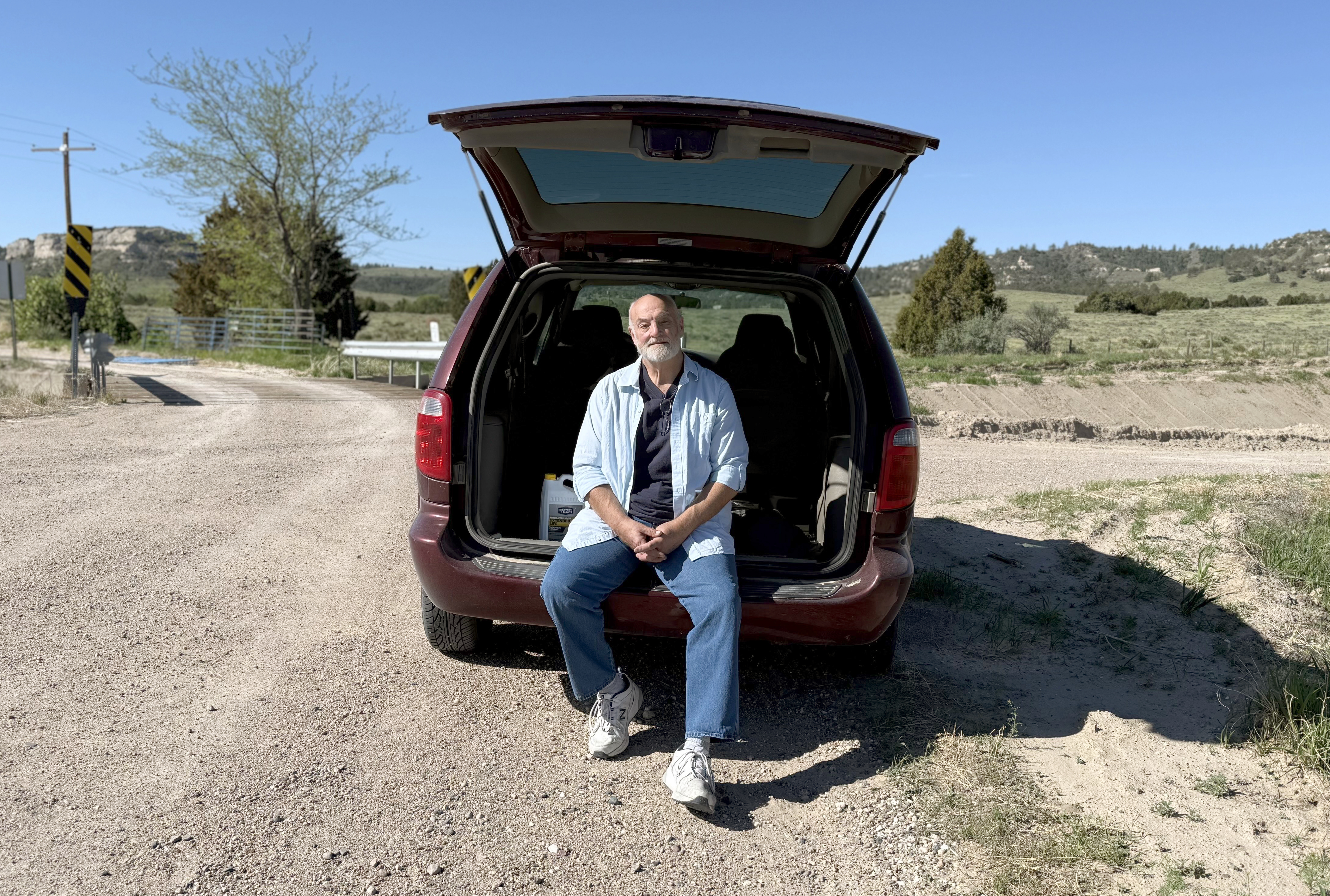 Roger McDonald sits in the back of his preferred rural mail delivery vehicle, a Dodge Caravan, on a gravel road along his 150-mile route outside Scottsbluff in northwestern Nebraska on May 11, 2025. The 61-year-old letter carrier worries about what would happen to his customers, his coworkers and himself if the Postal Service further curtailed service or was privatized.<br />(Nick Loomis / The Midwest Newsroom)