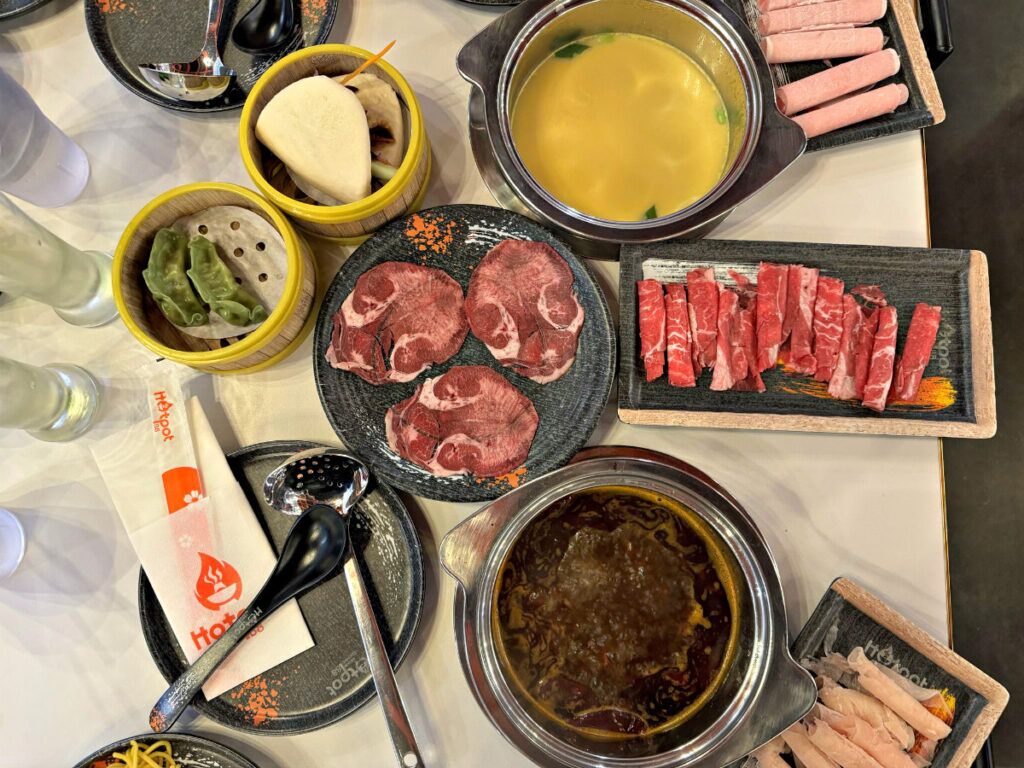An overview of a dining table at Hotpot 88 includes, clockwise from top left: vegetable dumplings, pork bao bun, Thai broth, pork, beef, chicken, Sichuan spicy broth and oxtail.<br />(Sarah Baker Hansen / Flatwater Free Press)