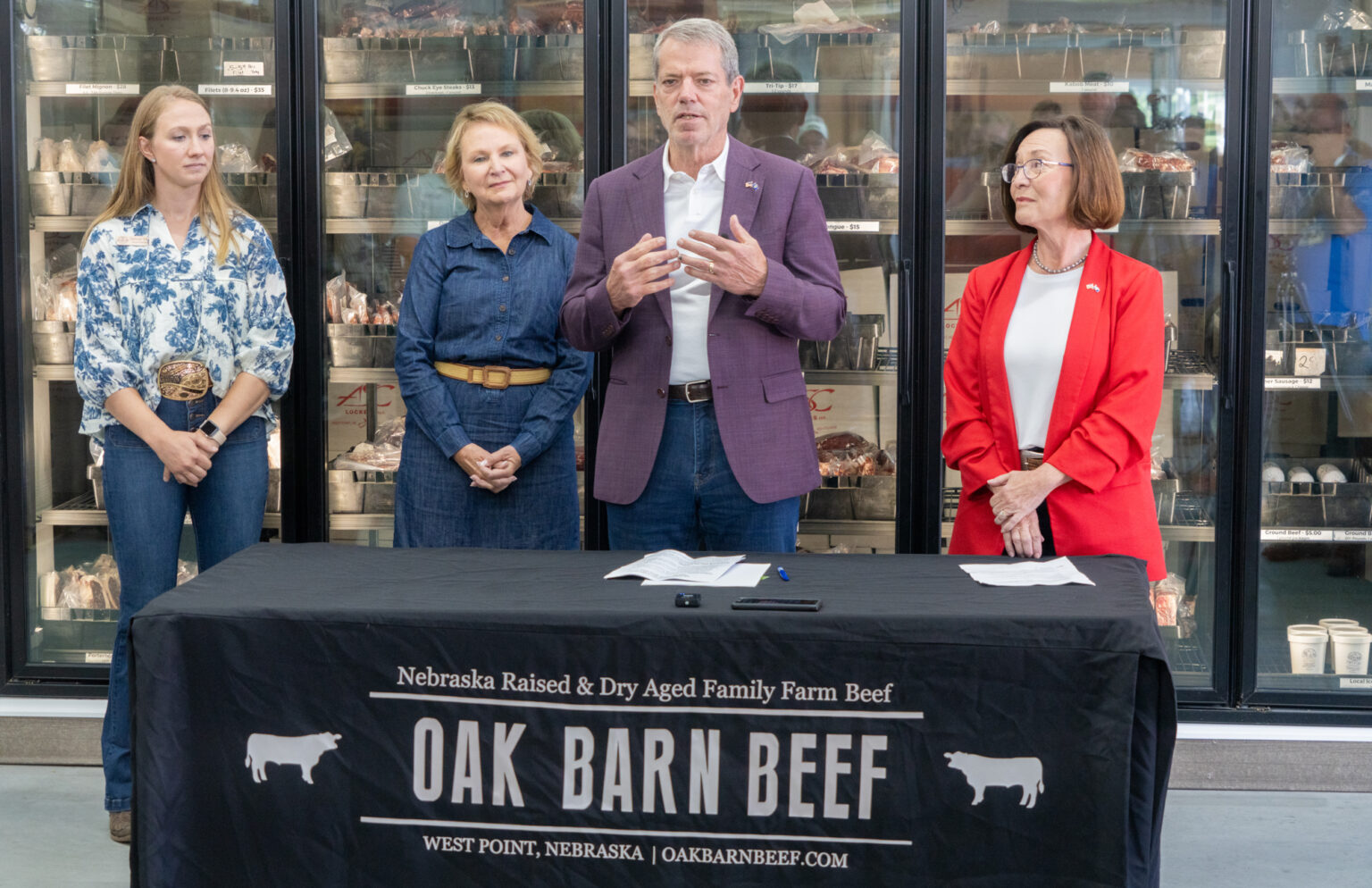 Gov. Jim Pillen (center) hosts a news conference at Oak Barn Beef in West Point announcing new regulations and future legislation to crackdown on “fake” or “lab-grown” meat in Nebraska on Thursday, Aug. 29, 2024. Behind him are, from left: Hannah Klitz, co-owner and co-operator of the family led Oak Barn Beef; Jeanne Reigle of Madison, a livestock producer and 2024 legislative candidate; and Director Sherry Vinton of the Nebraska Department of Agriculture.<br />(Zach Wendling / Nebraska Examiner)