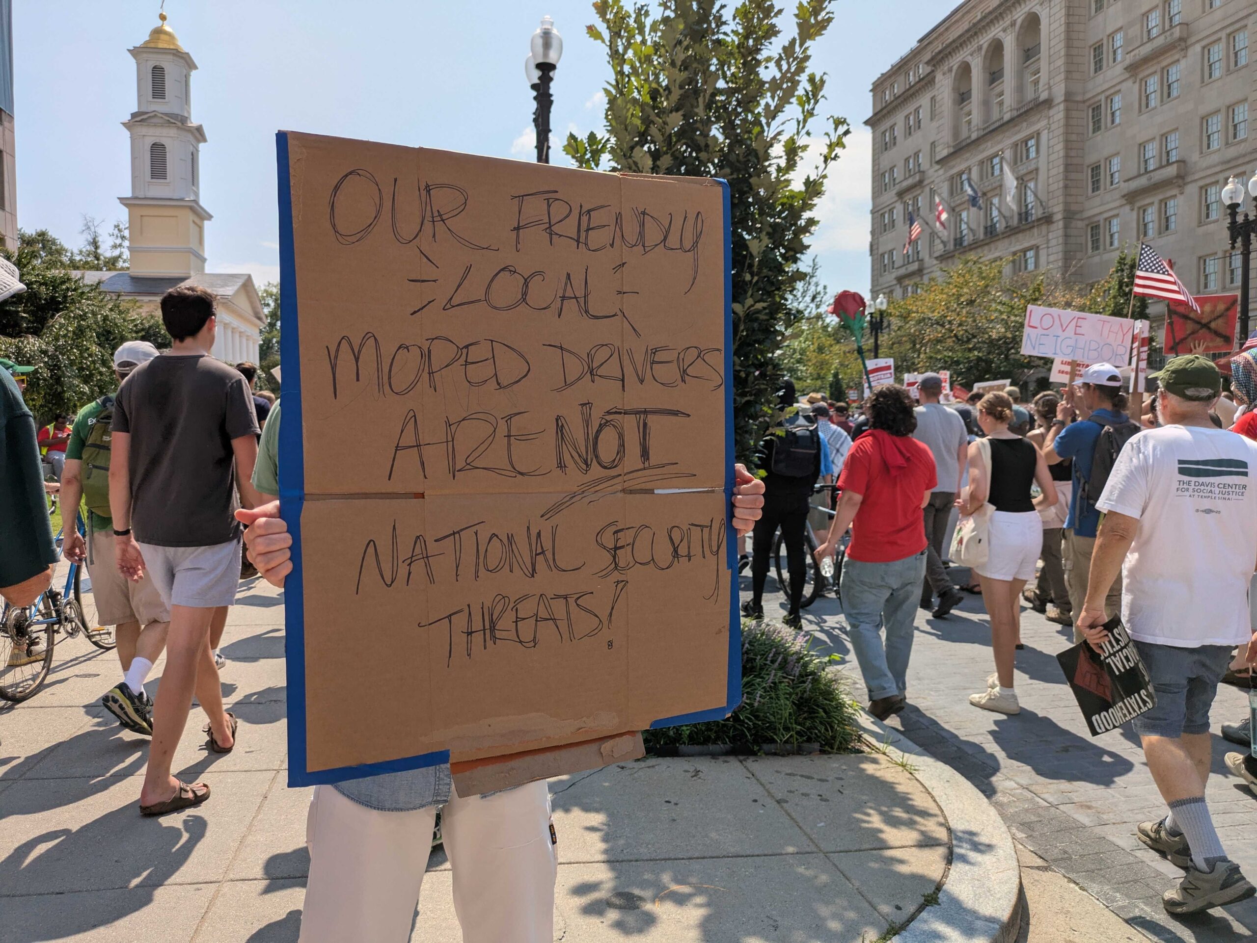 A demonstrator at a march on Sept. 6, 2025, protesting the Trump administration’s federalization of law enforcement and deployment of National Guard troops in Washington, D.C., held a sign on 16th Street NW defending local moped food delivery drivers.<br />(Ashley Murray / States Newsroom)