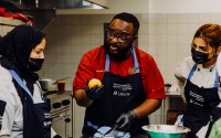 Djamil Djibril Bah-Traore (center) instructs Baaouine Naima (left) and Malalk Ashbalu (right) during a cooking class organized by House of Bah, the catering-company-turned-nonprofit that Bah-Traore started in 2015. Through classes like this one on Dec. 16, 2023, in Omaha, Bah-Traore has helped train more than 30 immigrants how to cook in a professional setting. 
(Joshua Foo / Flatwater Free Press)
