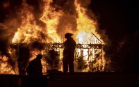Firefighters stand on top of a fire apparatus as they work to set up a deck gun while silhouetted by fire at an abandoned commercial building in Woodstock, Va., on Friday, Aug. 12, 2022. (Rich Cooley / Northern Virginia Daily via AP)