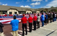 A dedication event for the Dunham House in Omaha, a long-term assisted living facility for veterans severely maimed in combat, kicked off Friday with a flag ceremony. The 30-unit residential complex is in the background. 
(Cindy Gonzalez / Nebraska Examiner)