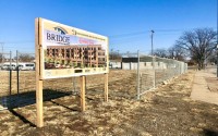 Project site of The Bridge Flats in the Frontier District of Olde Towne Bellevue. A fence surrounds the area, which remains a grassy lot where the old City Hall used to be.  (<a href="https://nebraskaexaminer.com/author/cindygonzalez/">Cindy Gonzales</a> / Nebraska Examiner)