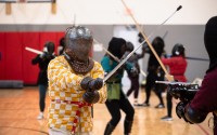 Participants at the Nebraska Swordfighters Guild’s January Fight Camp wear colorful gambesons – traditional padded or quilted jackets that would have been worn under armor in medieval combat. The gambesons, along with gloves, gorgets (steel or leather garments that protect the neck) and masks help fighters stay safe during exercises and sparring. 
(Liz McCue / Flatwater Free Press)