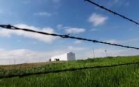 Pillen Family Farms Mt. Echo experiment shed is visible through the barbed wire fence along the property line with Neal and Bev Kemper’s farm on Monday, May 20, 2024, near St. Edward. Neal Kemper said Pillen Family Farms used the structure to try to kill bacteria in hog transport trailers with heat. 
(Rebecca S. Gratz / Flatwater Free Press)