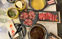 An overview of a dining table at Hotpot 88 includes, clockwise from top left: vegetable dumplings, pork bao bun, Thai broth, pork, beef, chicken, Sichuan spicy broth and oxtail. 
(Sarah Baker Hansen / Flatwater Free Press)